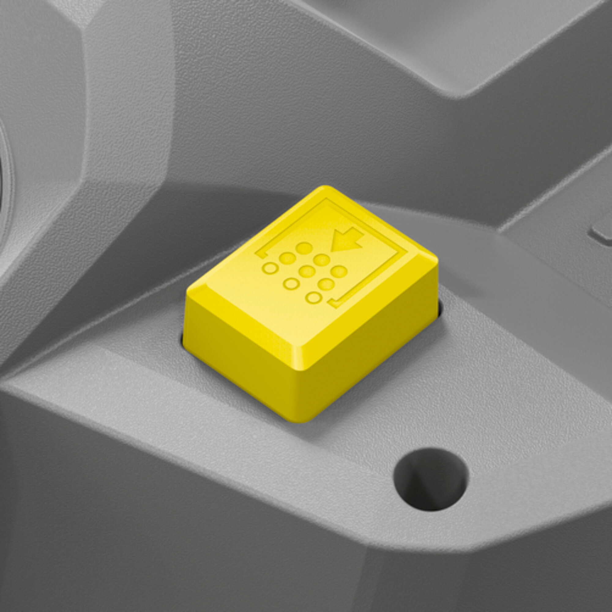 Żółty przycisk na szarym urządzeniu. Przycisk ma strzałki. Tło jest również szare.