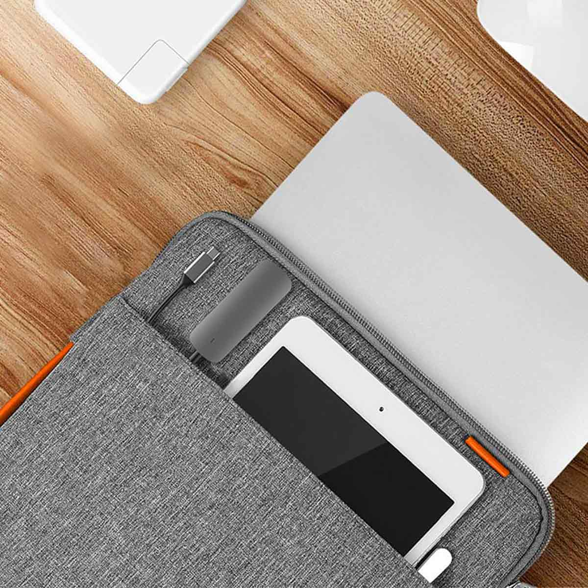 Laptop, Tablet und Zubehör in grauer Tasche auf Holztisch. Eine weiße Maus ist sichtbar.