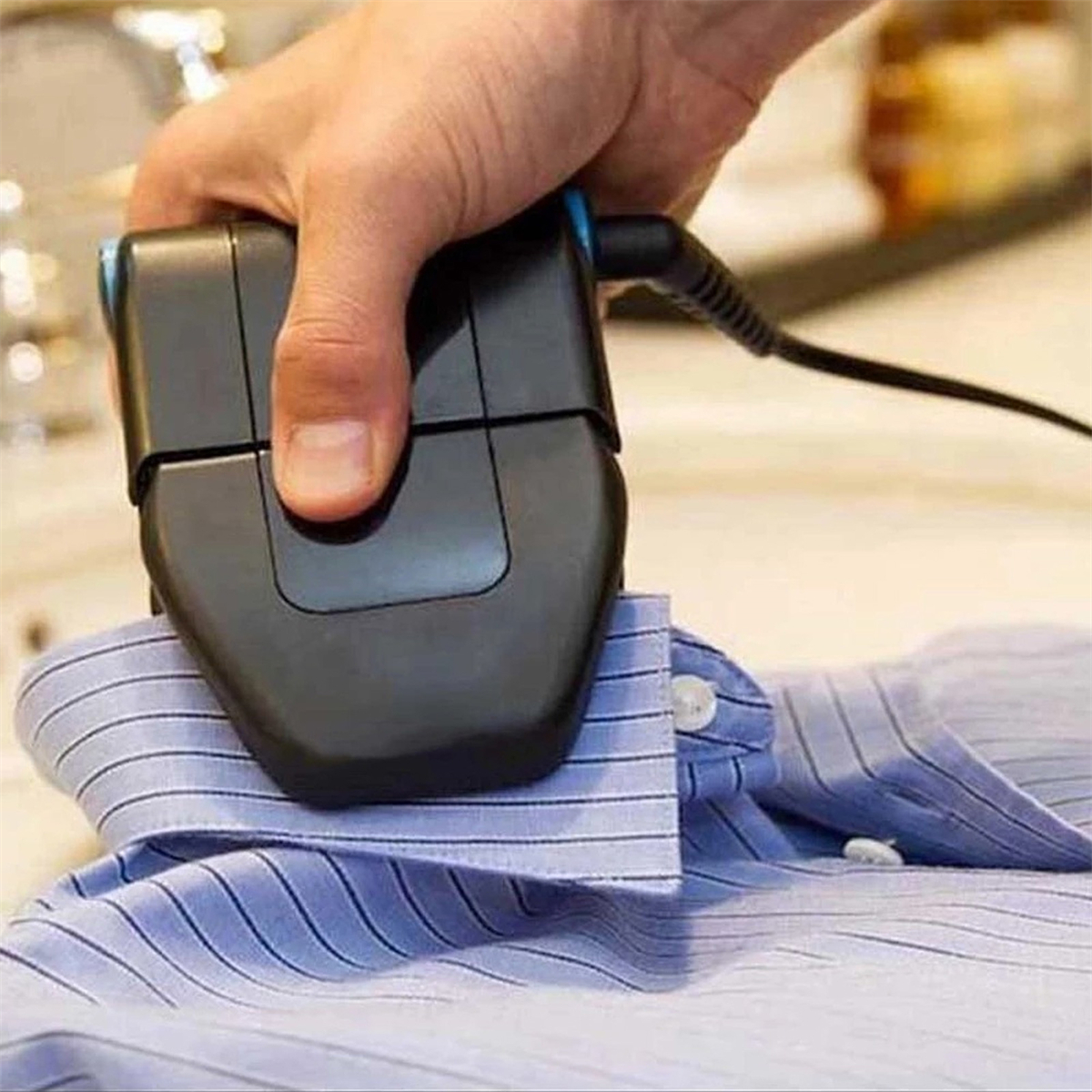 Eine Person bügelt ein blau gestreiftes Hemd mit einem kleinen schwarzen Bügeleisen.