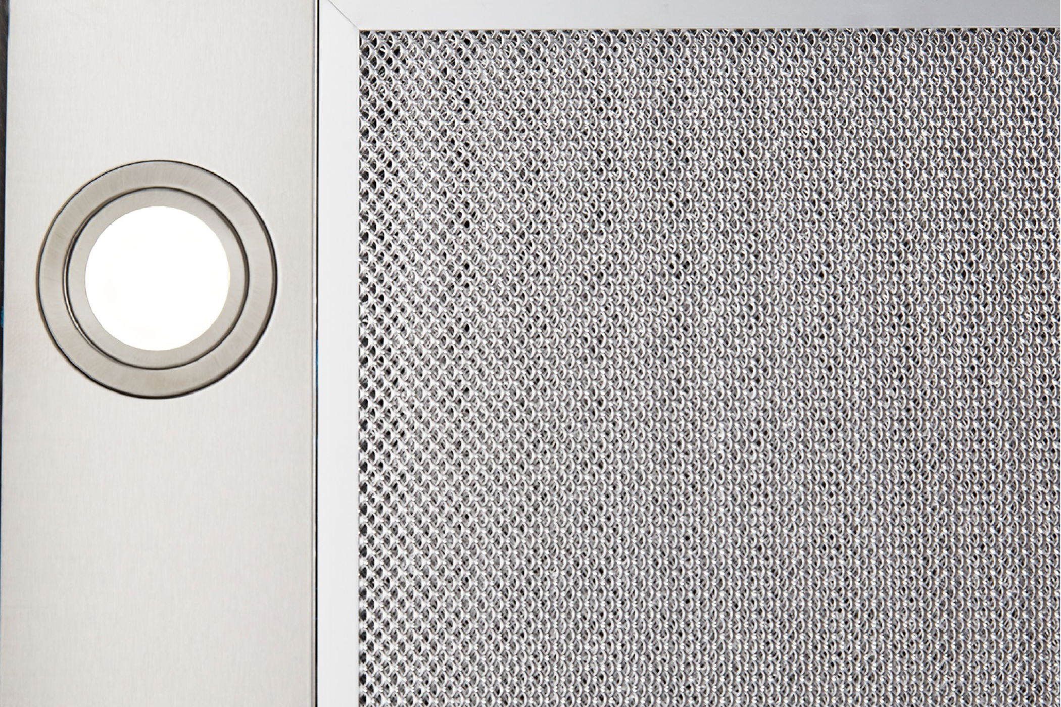 Close up of a silver range hood with a light and a metal mesh filter. Chrome accents.