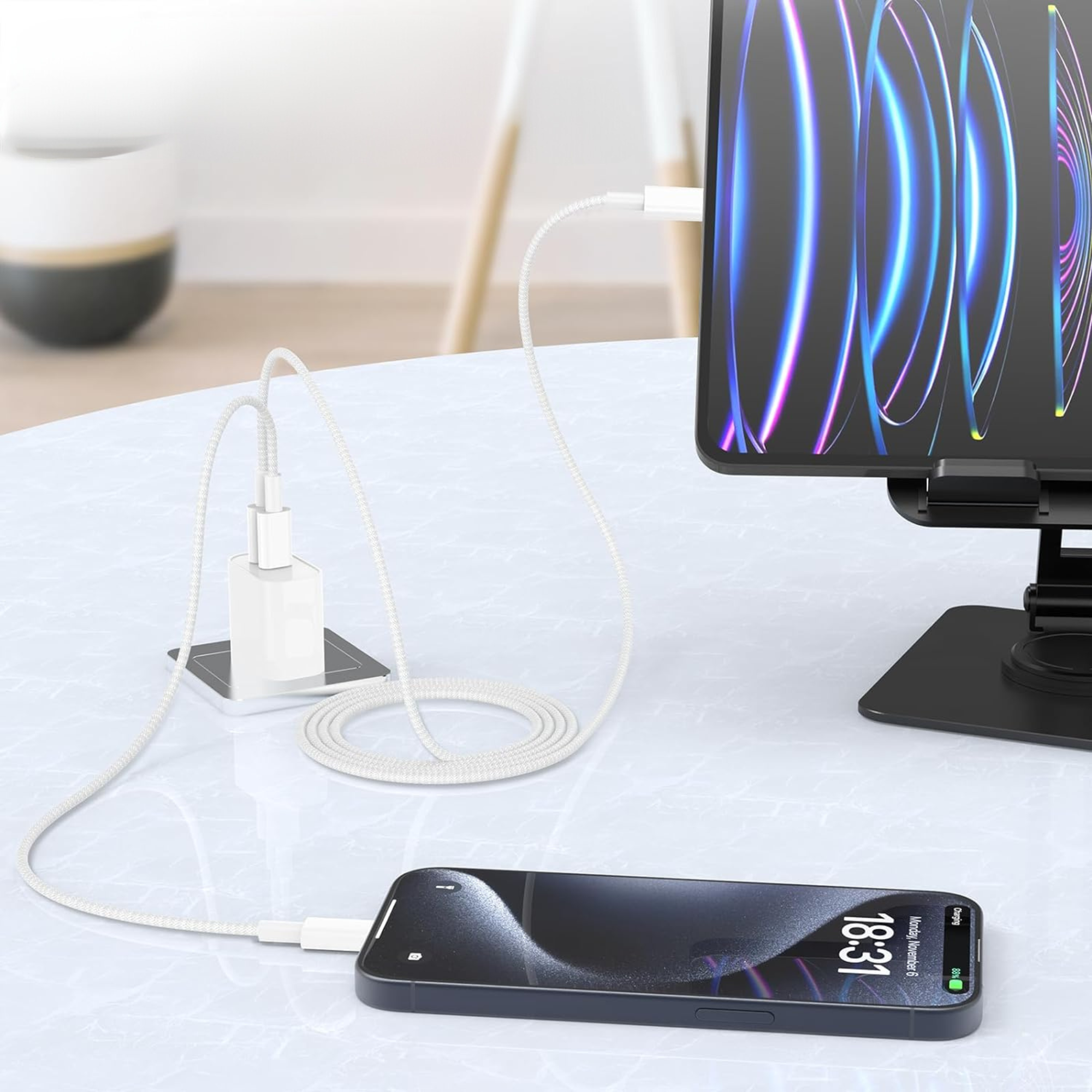 Un telefono è in carica. Un caricatore e un cavo sono su un tavolo. Un tablet è collegato a un supporto.