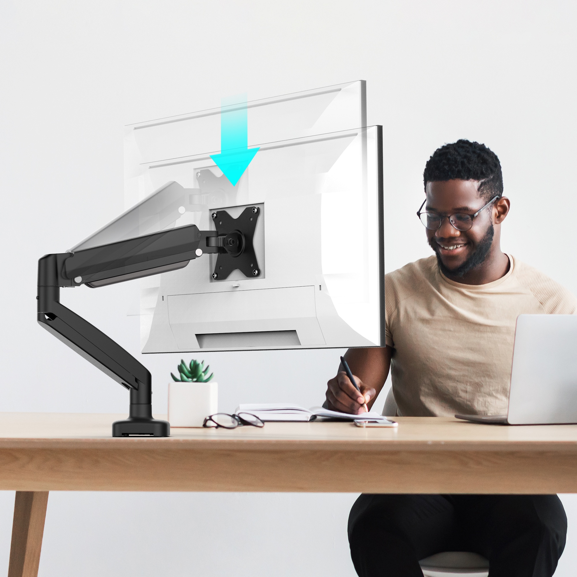 Homme travaillant sur ordinateur avec bras de moniteur. Bureau avec plante et lunettes. Fond clair.