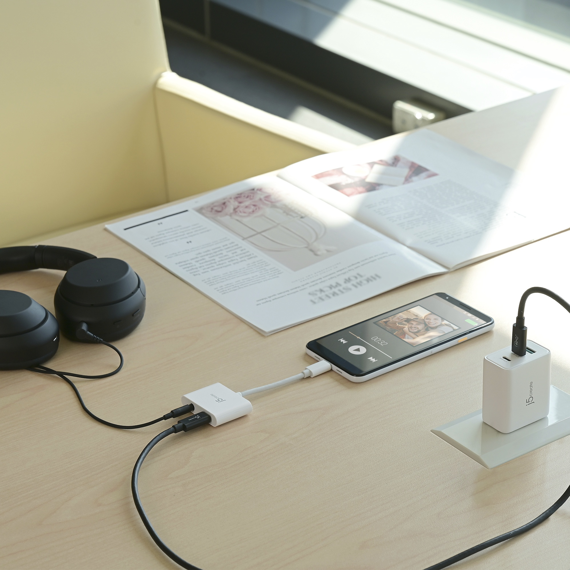 Teléfono con música, conectado a cargador y auriculares. Mesa de madera beige.