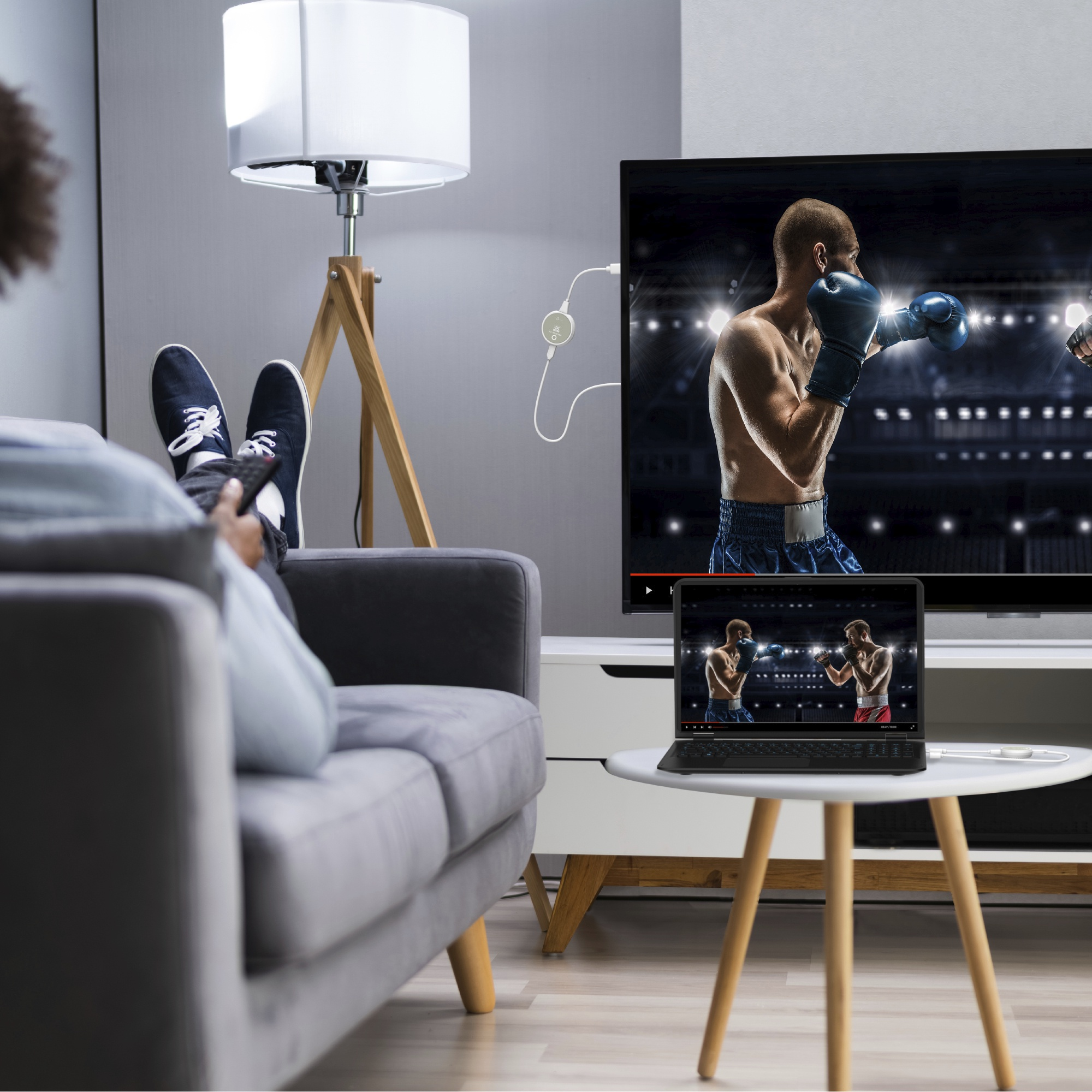 Person schaut Boxen im Fernsehen mit einem Laptop, der das gleiche Match zeigt. Eine Lampe steht daneben.