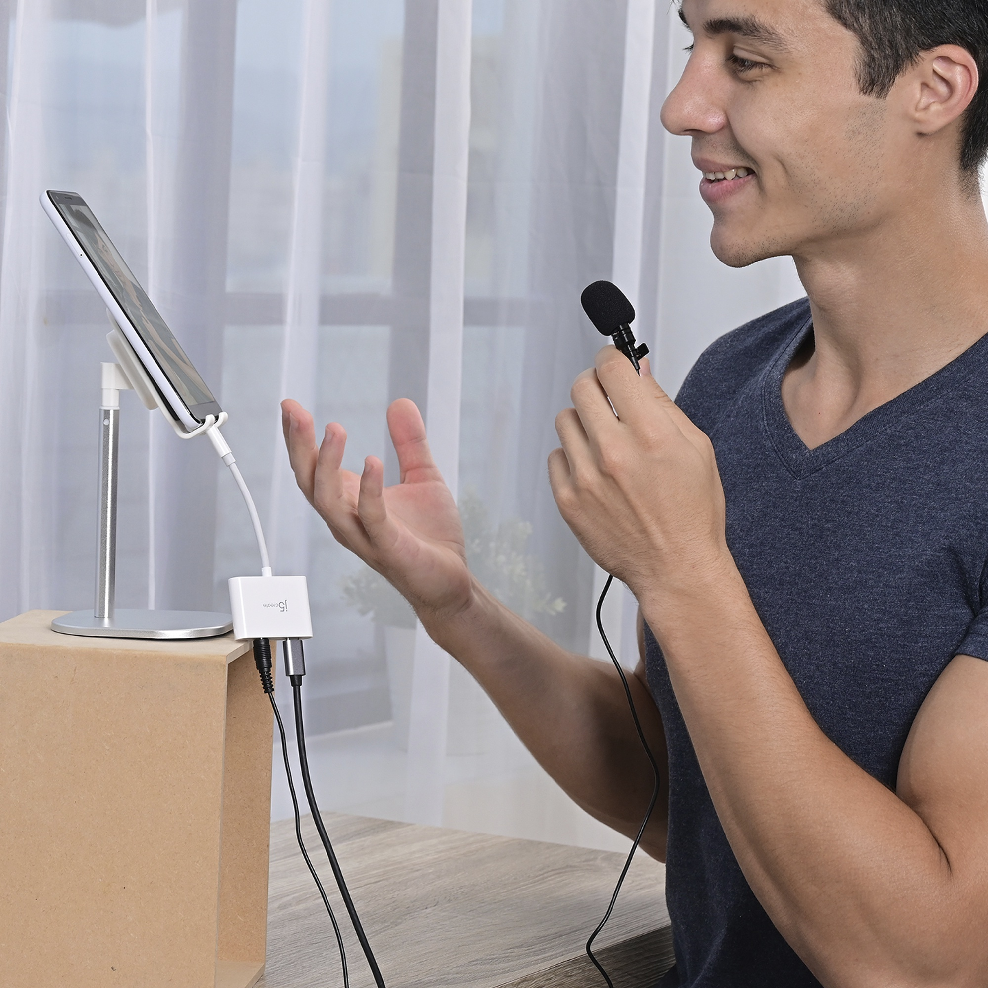Un hombre sosteniendo un micrófono, hablando a un teléfono en un soporte. Una caja de madera en la parte inferior.