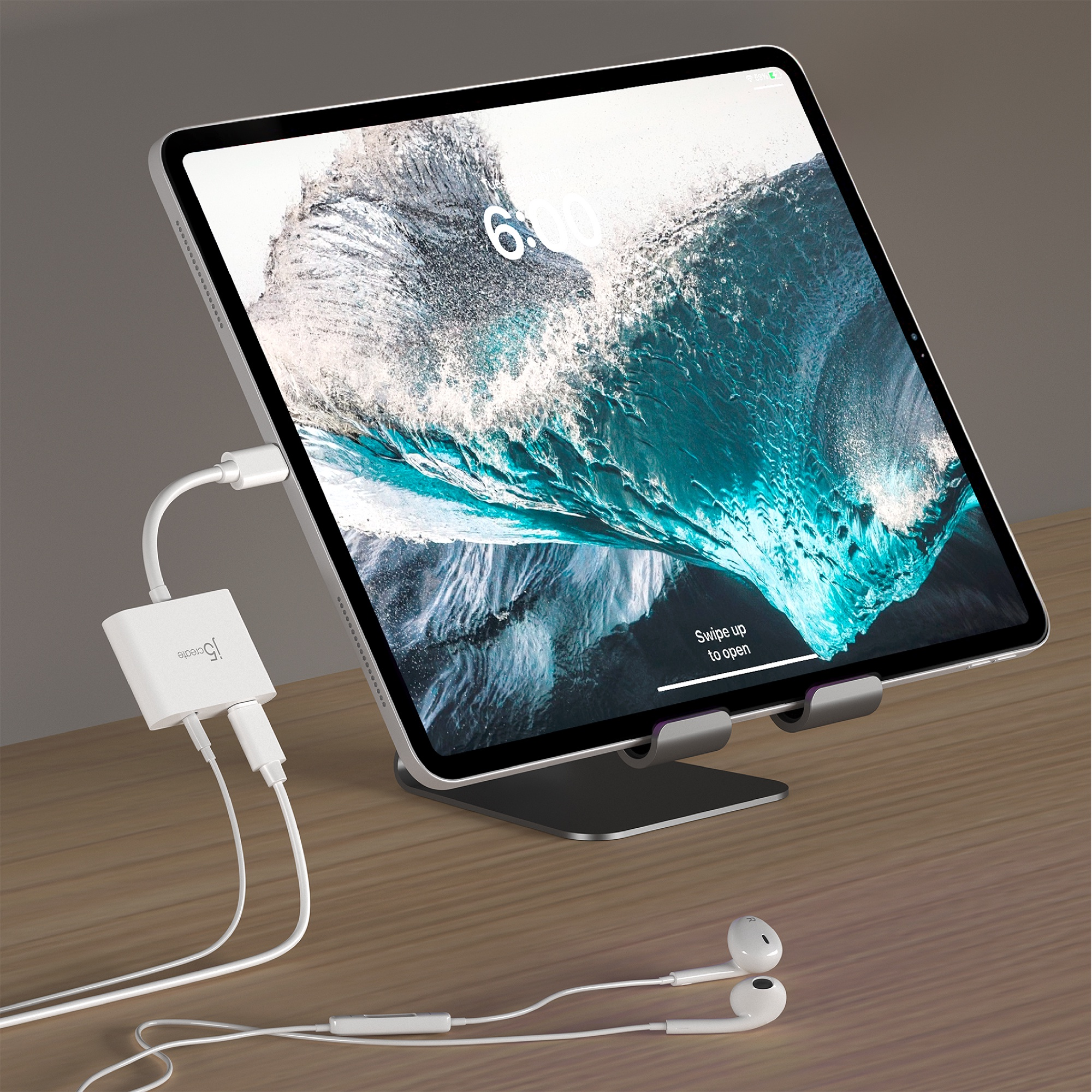Tableta en soporte, conectada a un adaptador y auriculares. La pantalla muestra una imagen de la naturaleza.