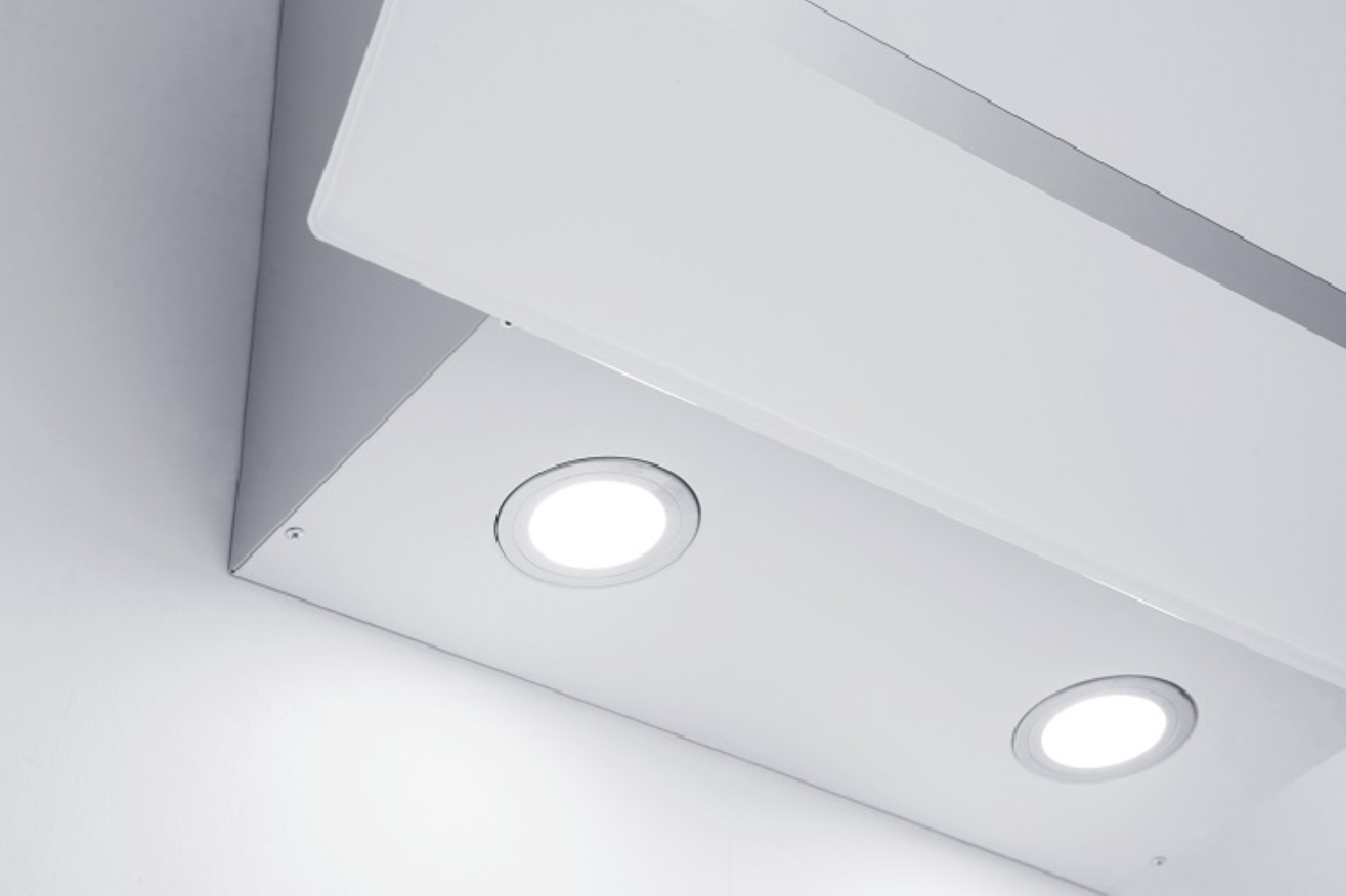 Laaghoekopname van een witte afzuigkap met twee cirkelvormige lampen tegen een witte muur.
