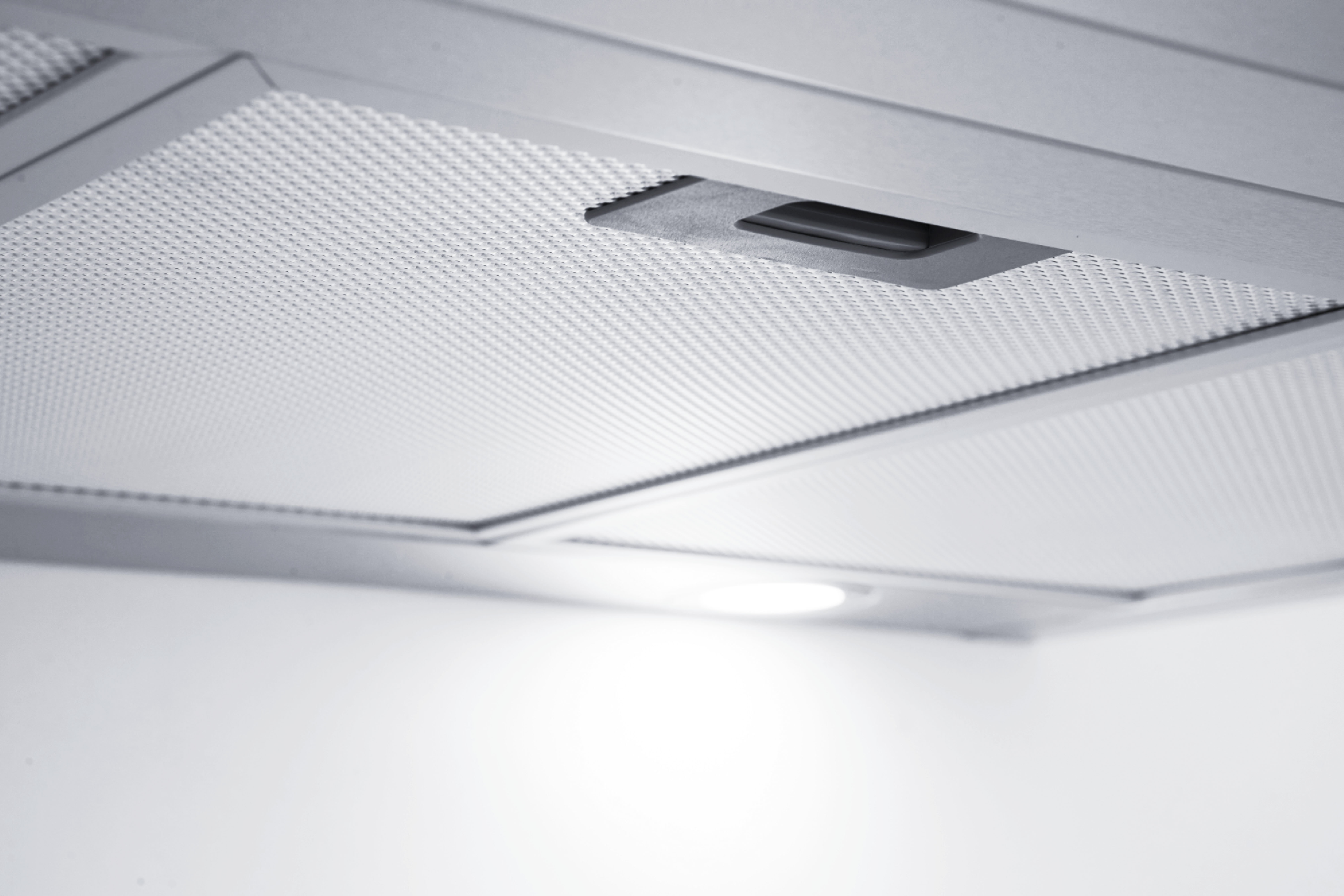 Close up of a kitchen hood with a metal mesh filter and a small light.
