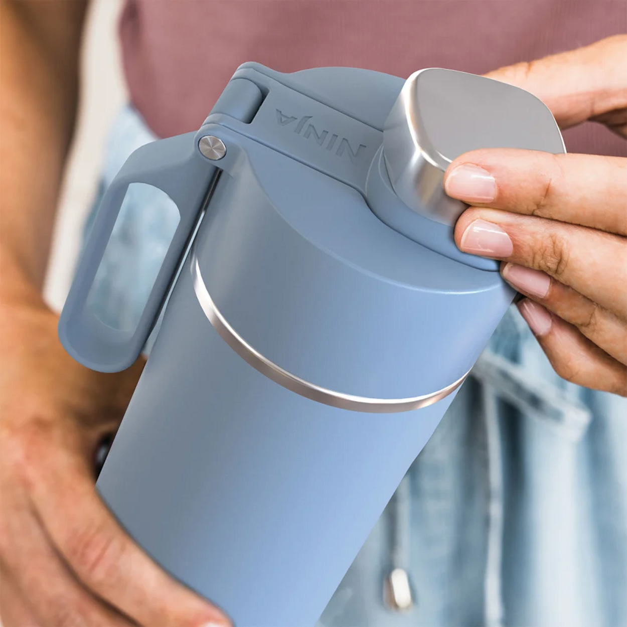 Mani che tengono una bottiglia d'acqua isolante blu con coperchio e manico argentati.