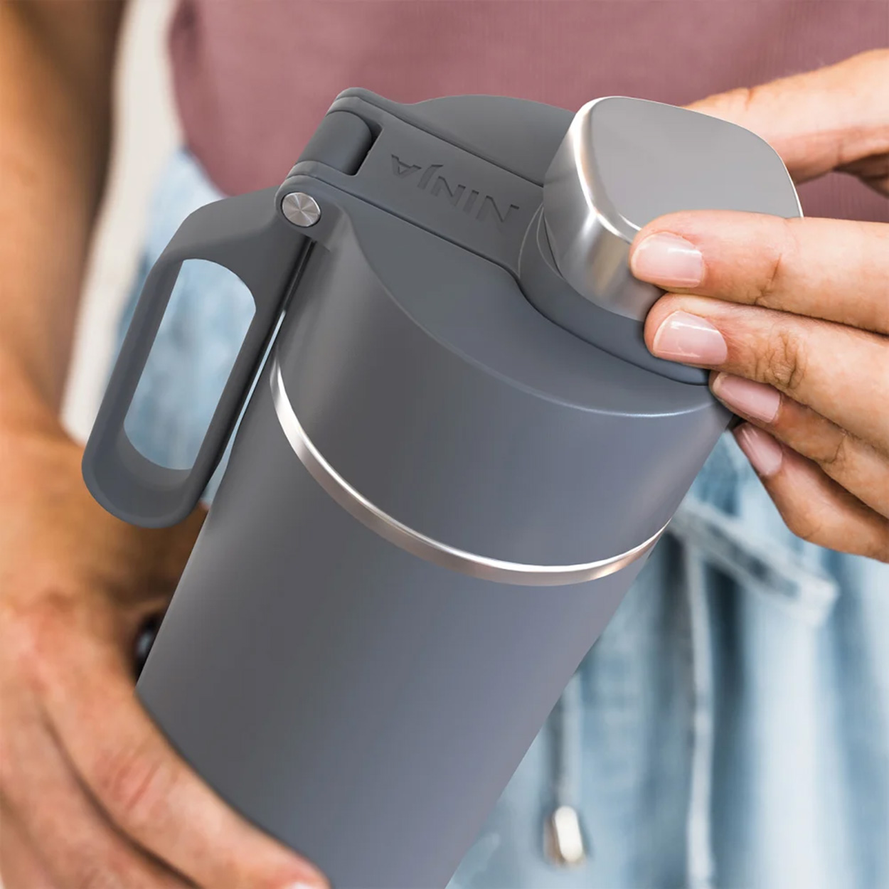 Eine Person hält einen grauen Ninja-Becher, wobei der Fokus auf dem Deckel liegt.