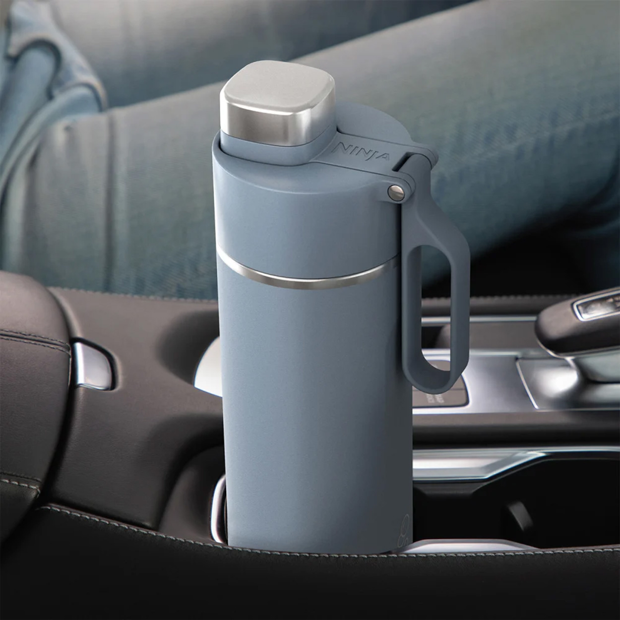 Una bottiglia d'acqua blu con manico nel portabicchieri di un'auto. Interno auto visibile.