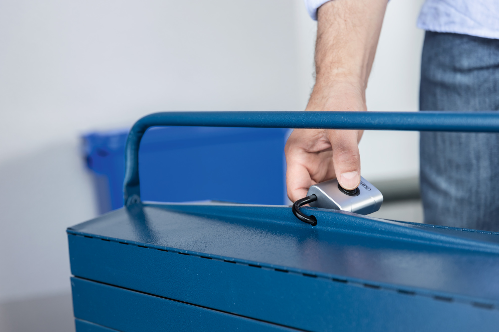 La mano di una persona è su una cassetta degli attrezzi blu. La mano tiene un lucchetto argentato.