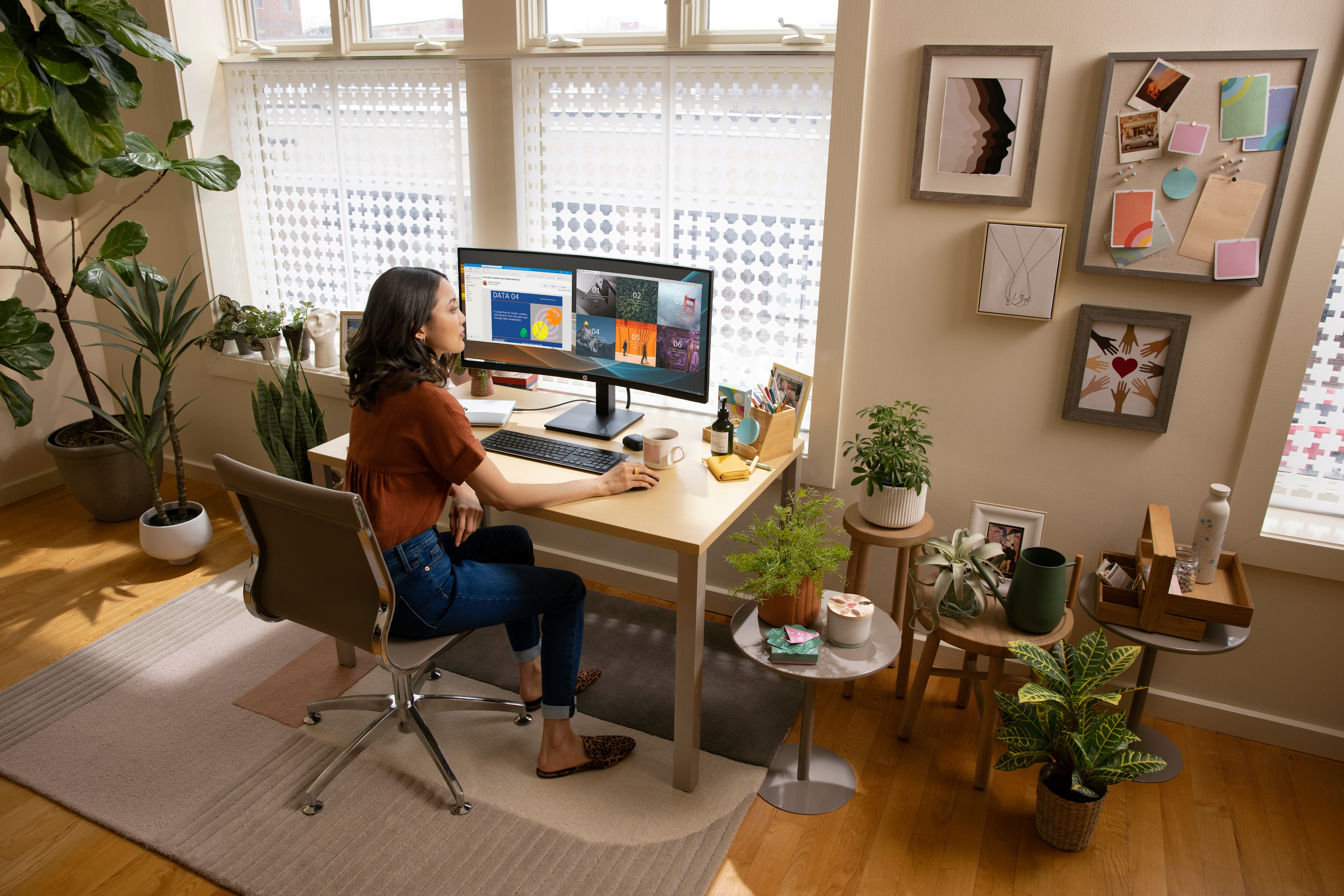 Kobieta pracująca przy biurku z dwoma monitorami, otoczona roślinami i artykułami biurowymi.