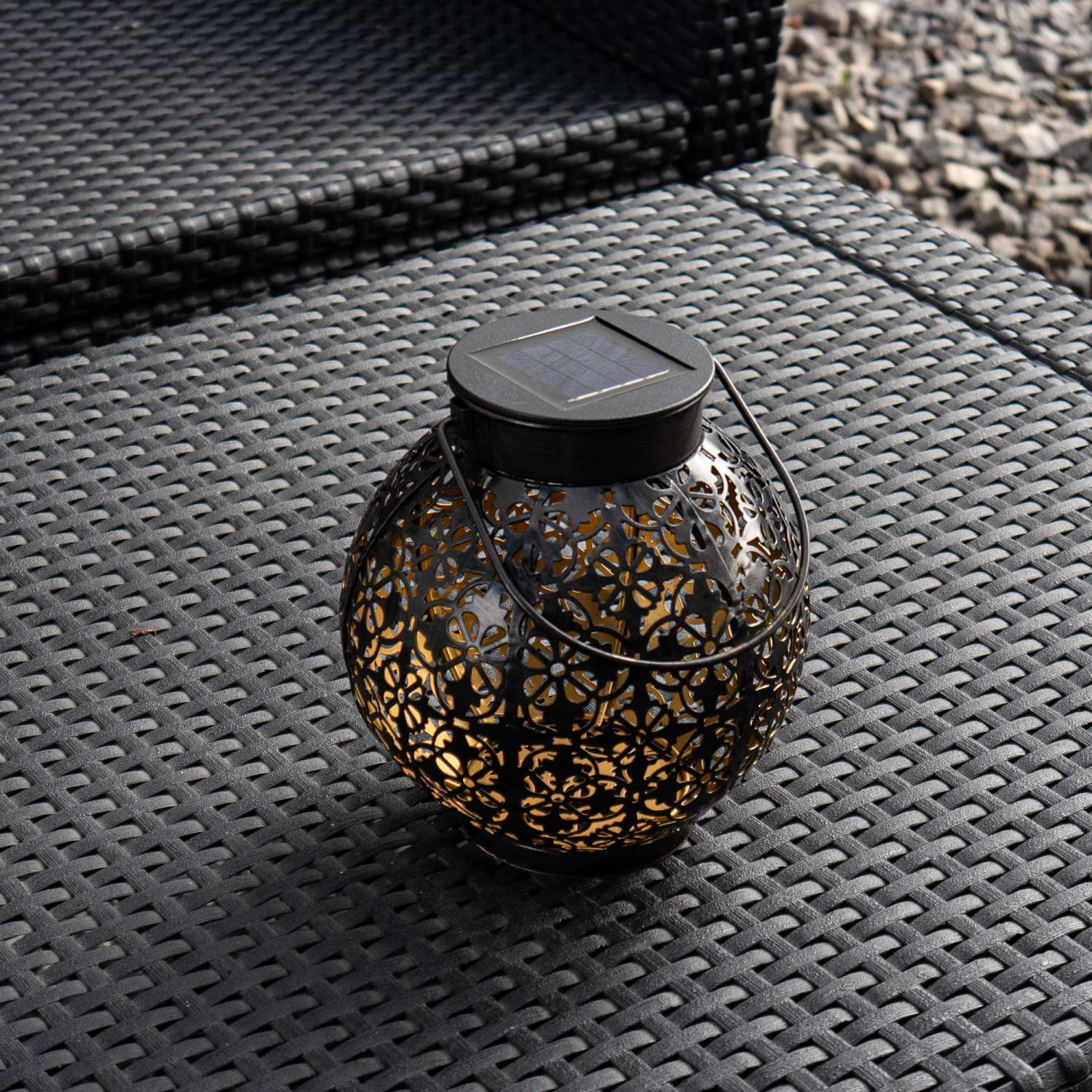 Schwarze Solar-Laterne mit floralem Muster auf einem schwarzen Korbtisch. Runde Form mit Griff.