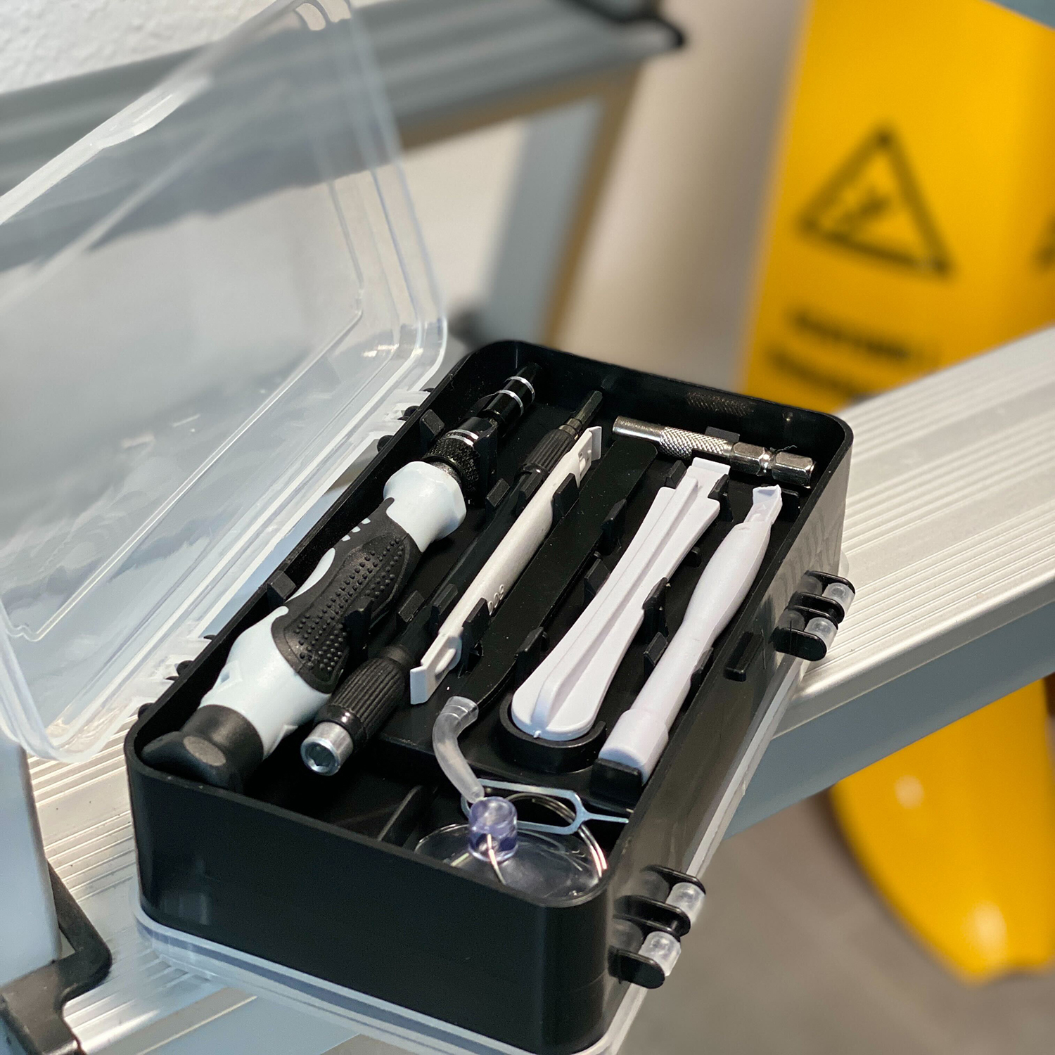 Ein schwarzer Werkzeugkasten mit verschiedenen Werkzeugen darin, geöffnet, auf einer Metalloberfläche.