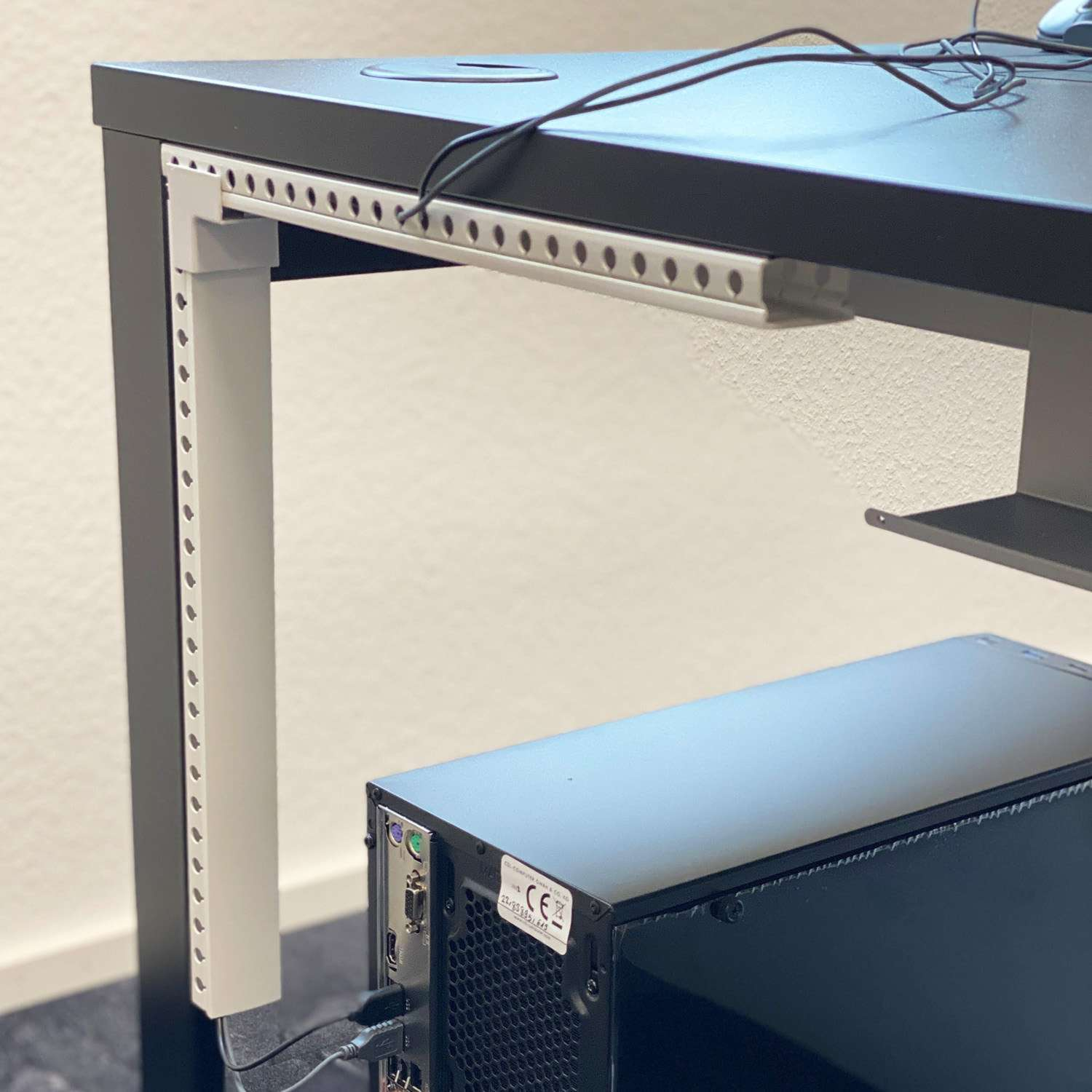 Schwarzer Schreibtisch mit Computergehäuse darunter. Weißer Halter für Kabel.