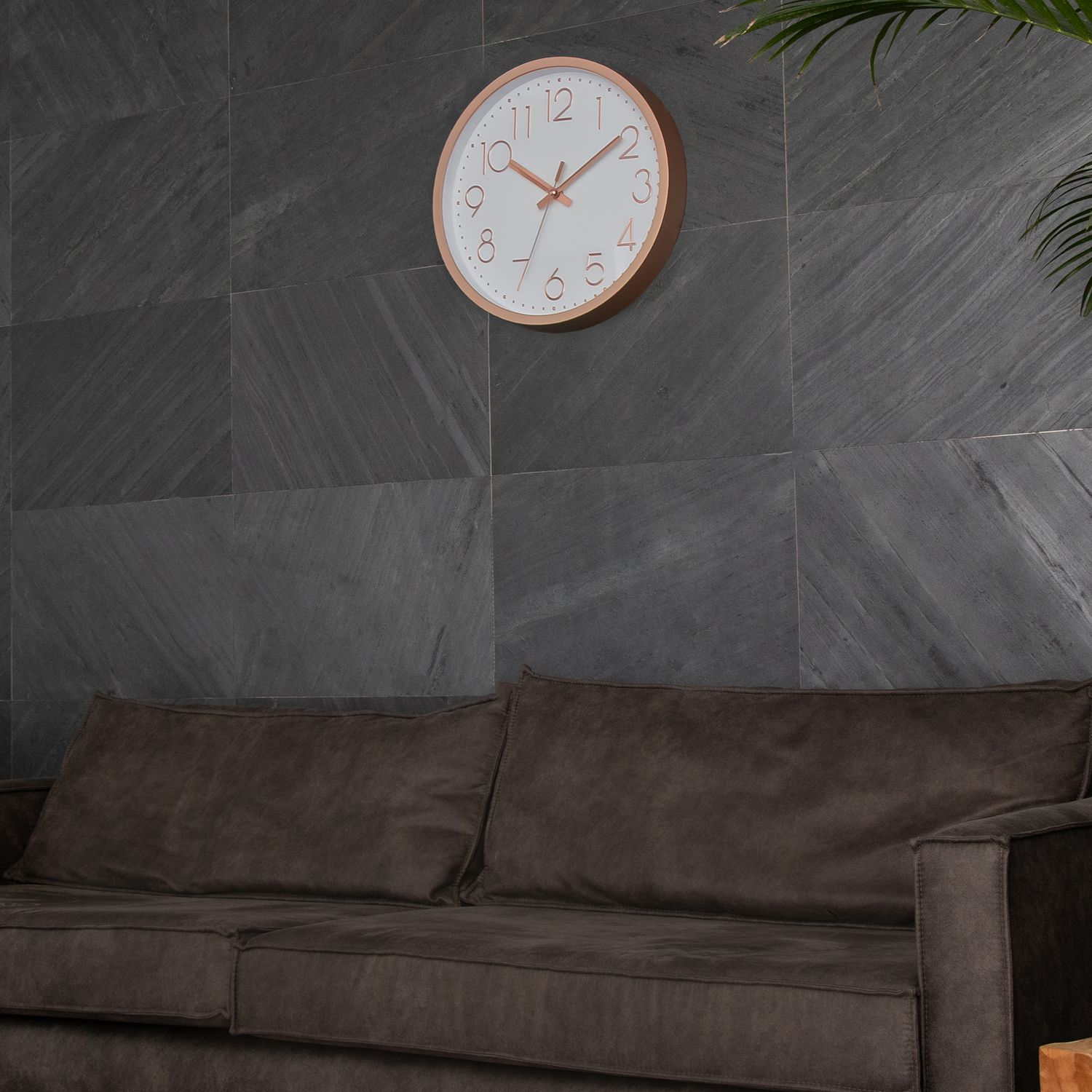 Runde Uhr an grauer gefliester Wand über einem braunen Sofa.