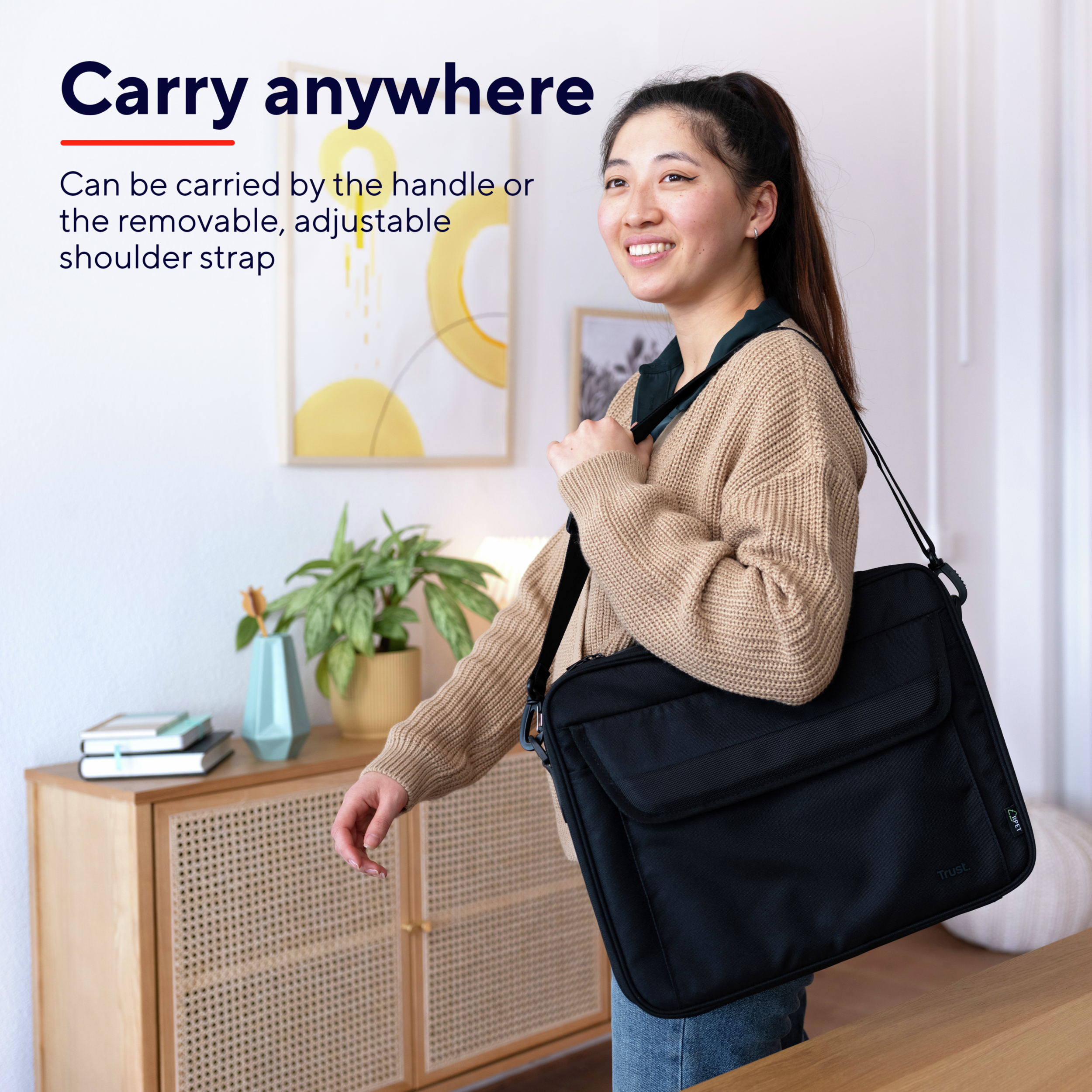Une femme souriante porte un sac messager noir. Le sac a une poignée, une bandoulière et un rabat.
