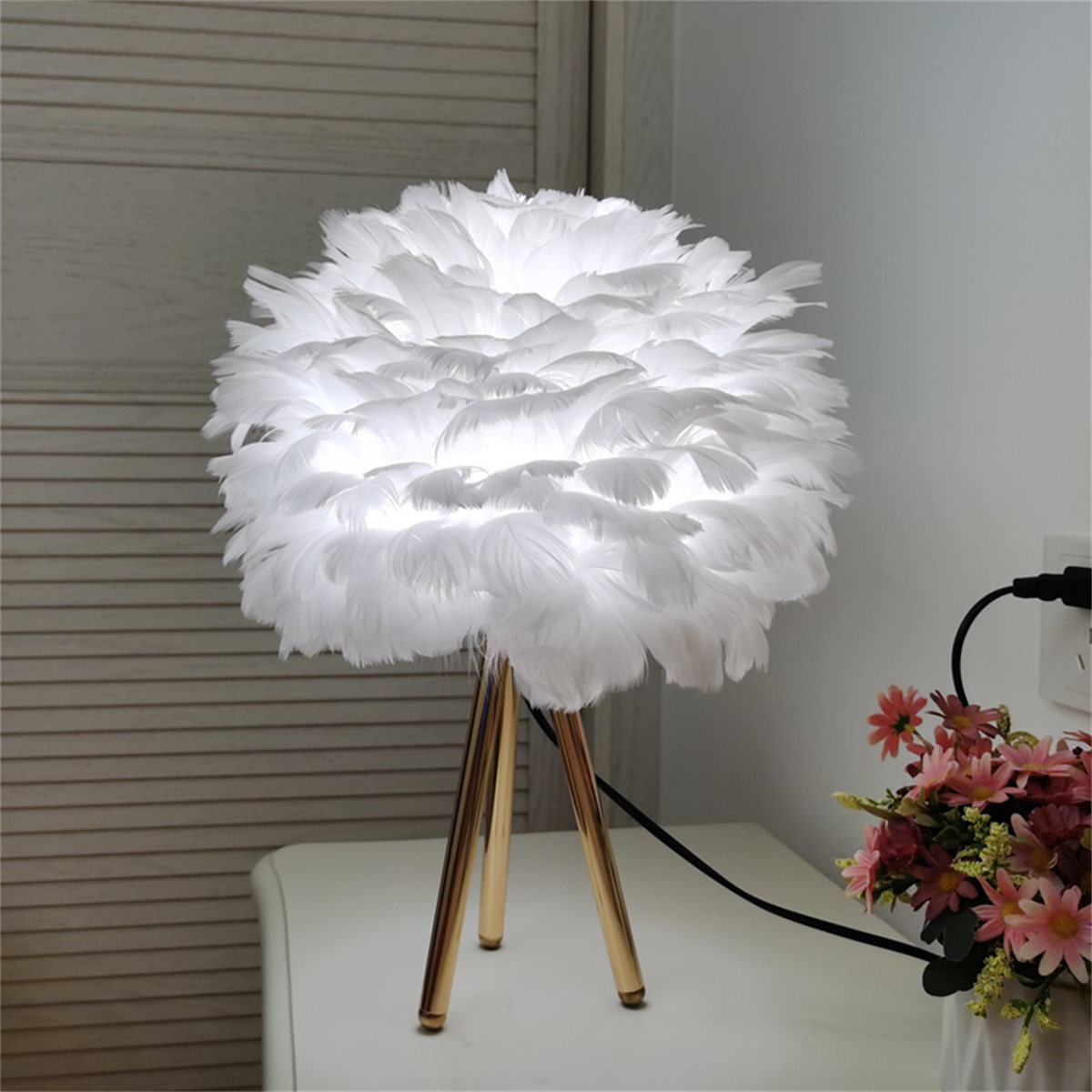 Weiße Federlampe auf weißem Tisch mit Blumen.