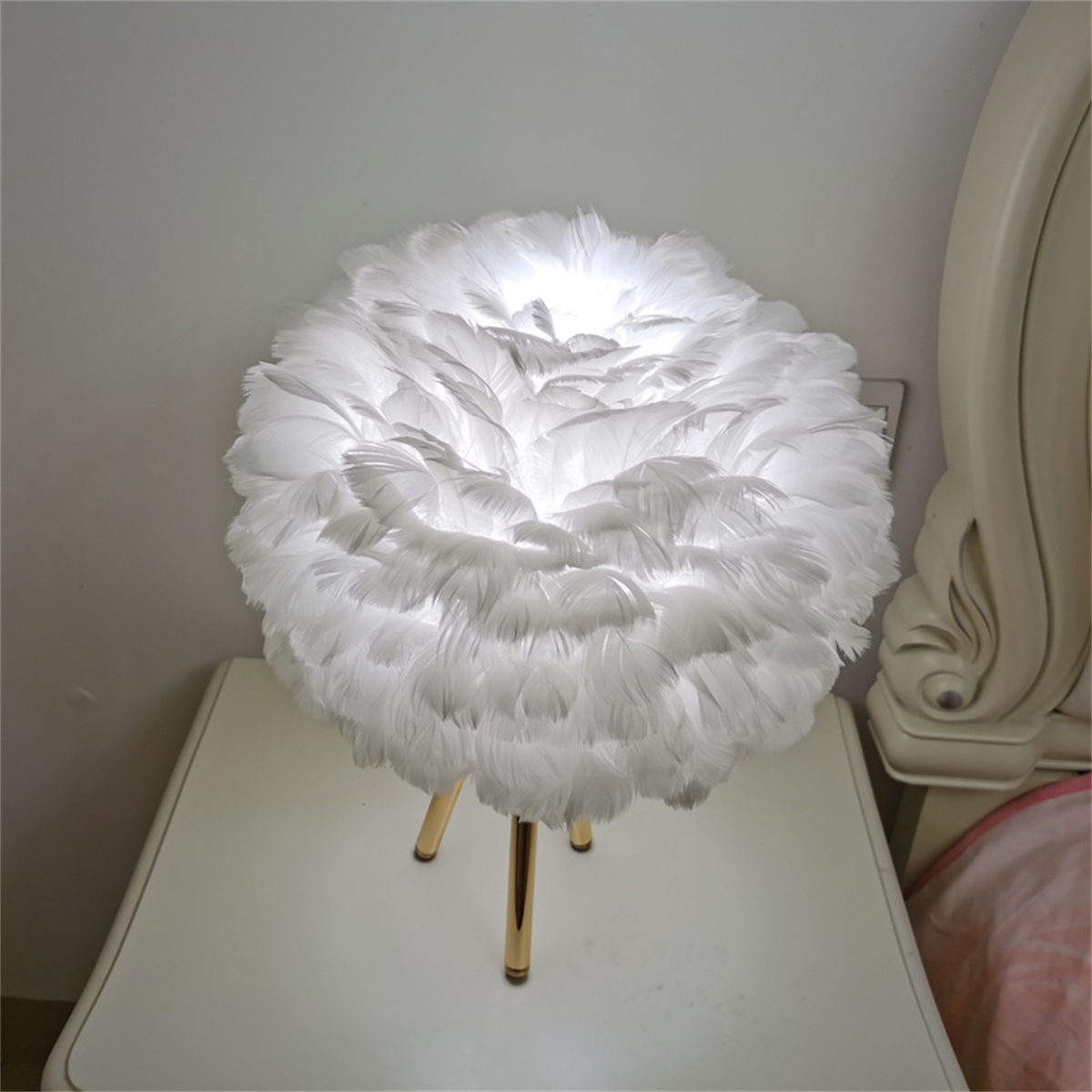 Weiße Federlampe auf einem Nachttisch. Goldene Beine. Weißer Wandhintergrund.