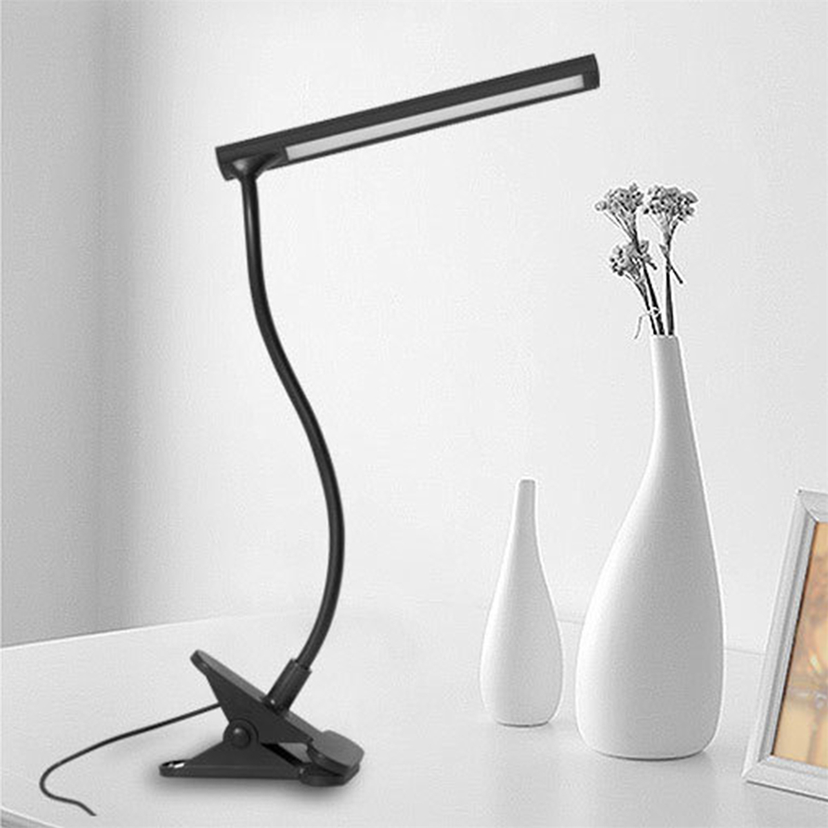 Eine schwarze Schreibtischlampe mit einem gebogenen Hals und eine Vase mit Blumen. Weißer Hintergrund.