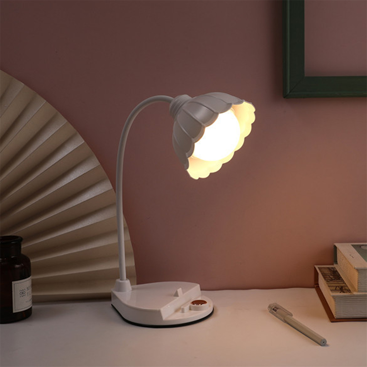 Weiße blütenförmige Lampe auf einem Schreibtisch mit Stift und Flasche.