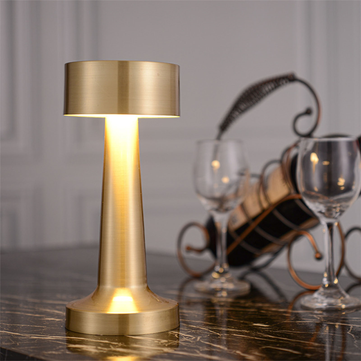 Eine goldfarbene Lampe auf dunkler Oberfläche, ein Weinregal und Gläser im Hintergrund.