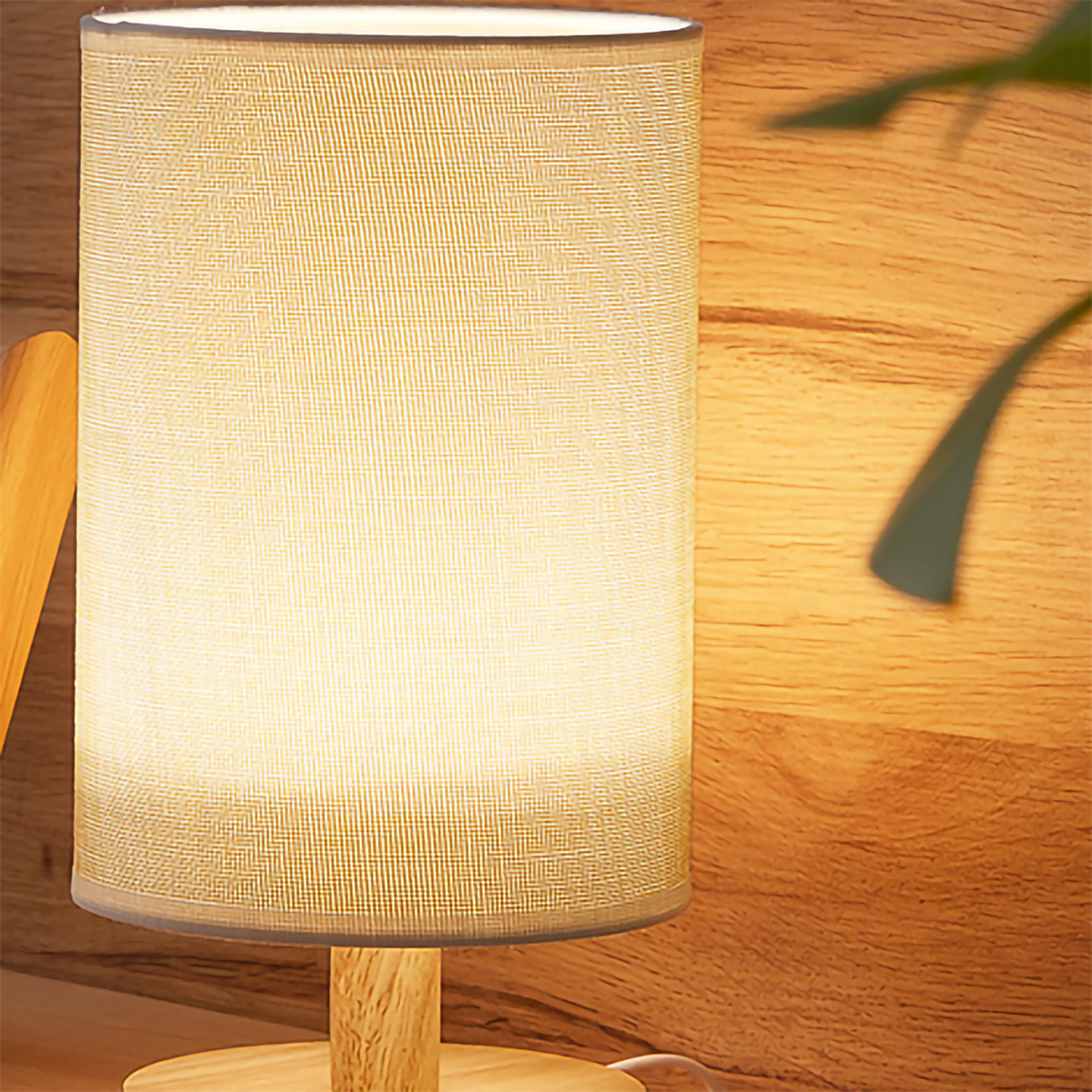 Eine Lampe mit beigem Lampenschirm und Holzfuß. Sie ist beleuchtet und steht auf Holz.