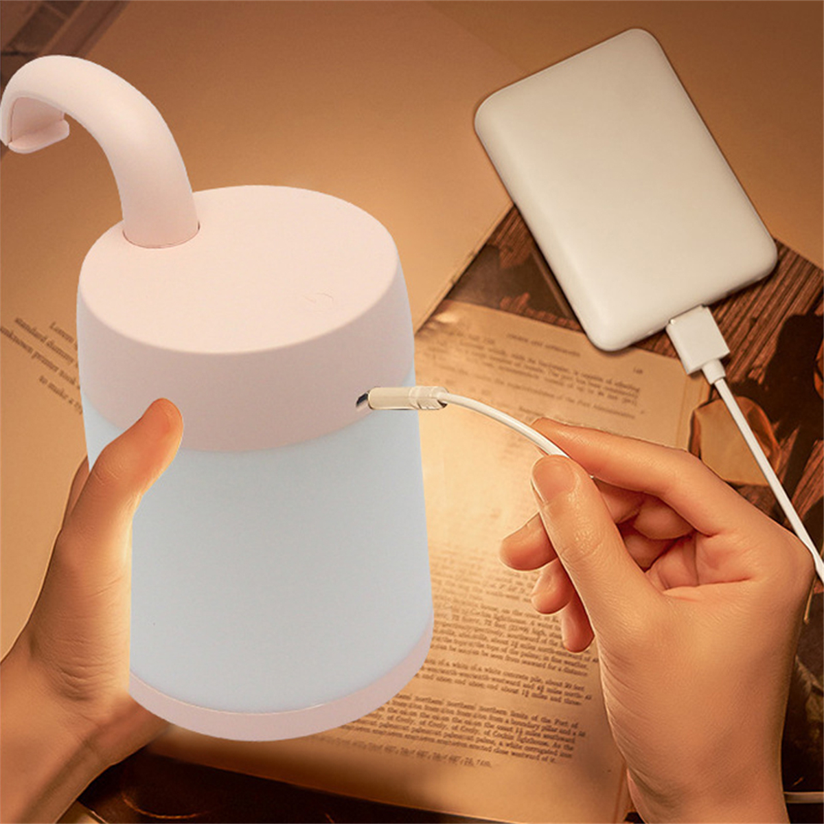 Eine rosa-weiße Lampe wird gehalten und ist mit einem weißen Ladegerät auf einem Buch verbunden.