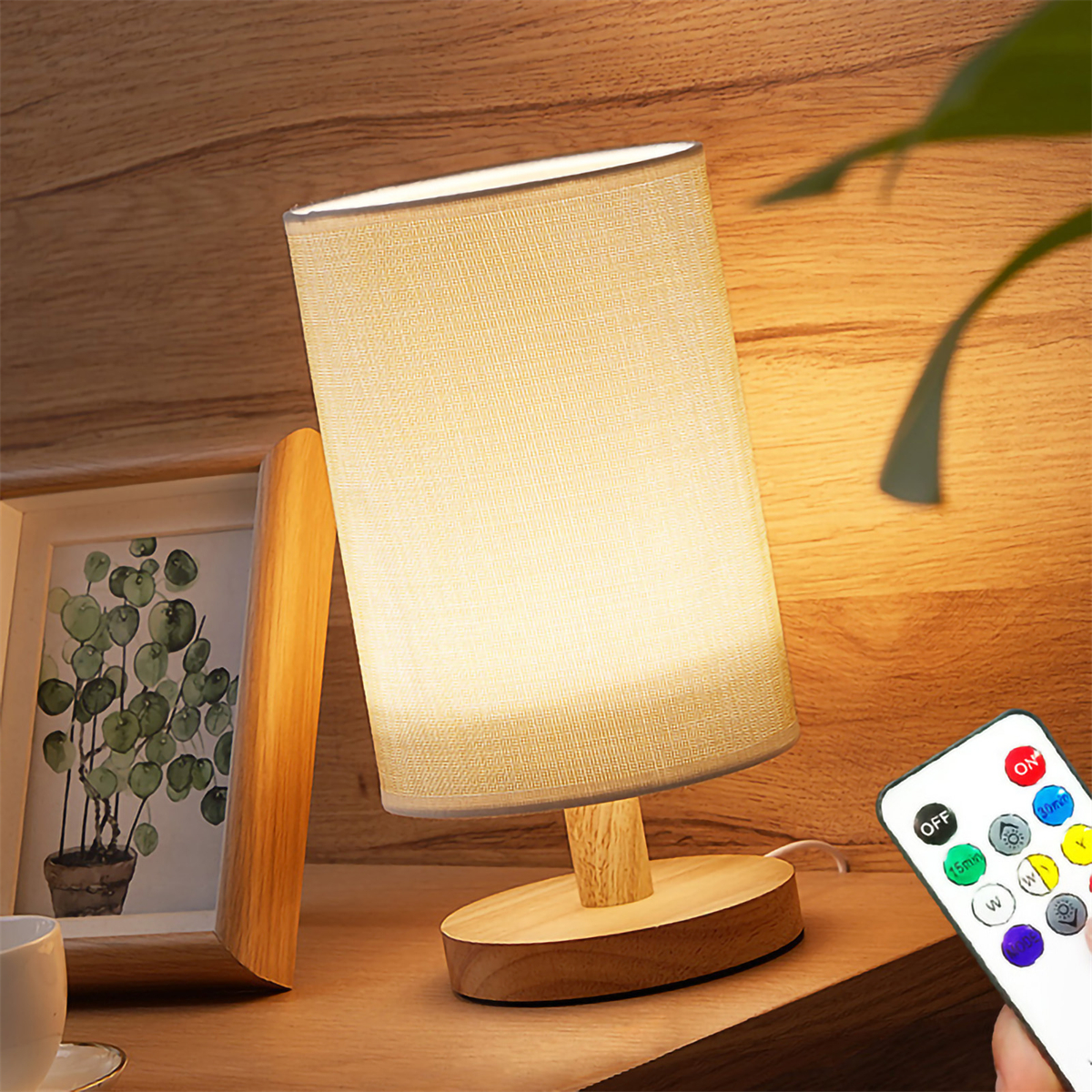 Eine Holzlampe mit zylindrischem Schirm auf einem Holzständer, schräg auf einer Holzoberfläche. Eine Fernbedienung ist im Bild.