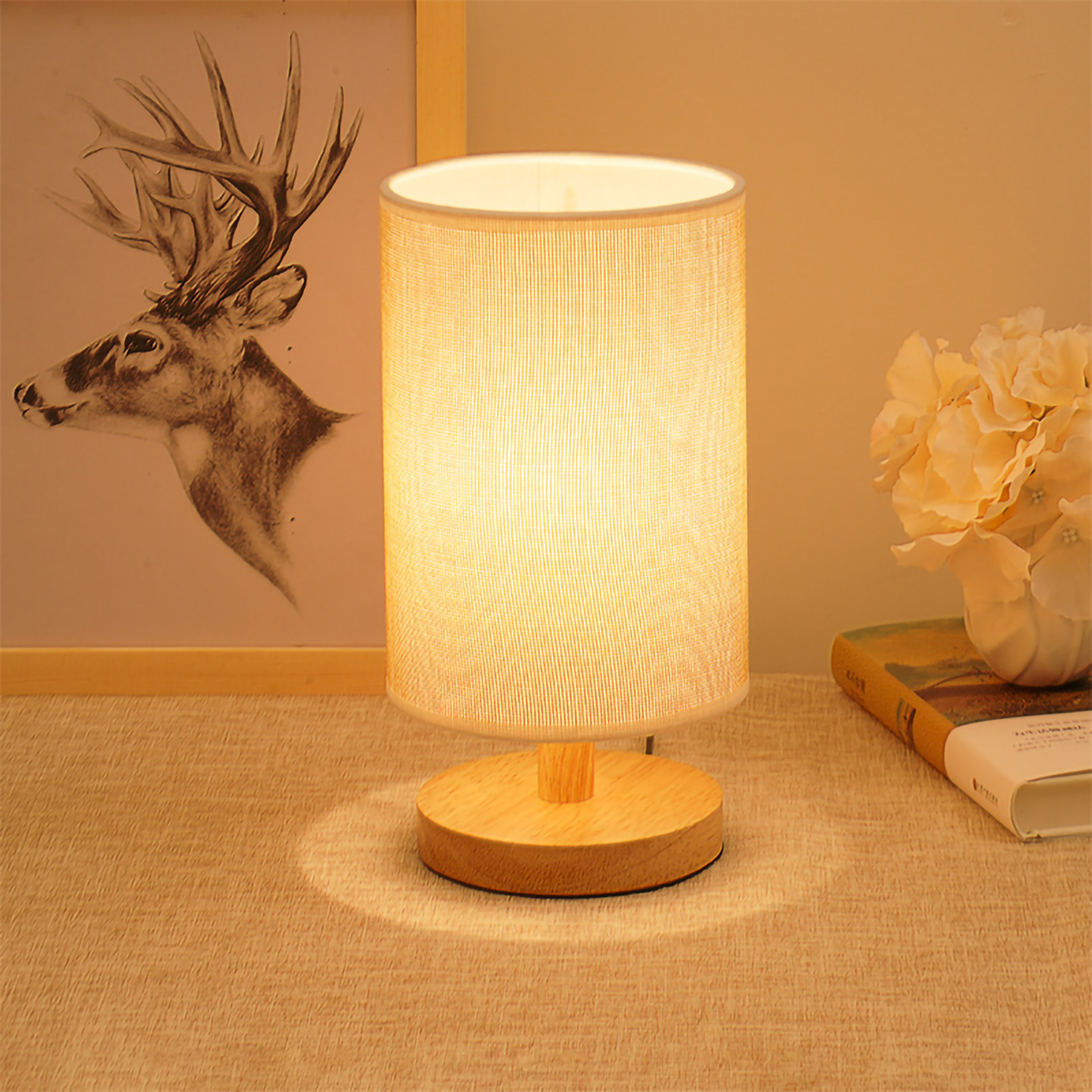 Beleuchtete Lampe mit Lampenschirm auf Holzsockel, neben Bild und Buch.