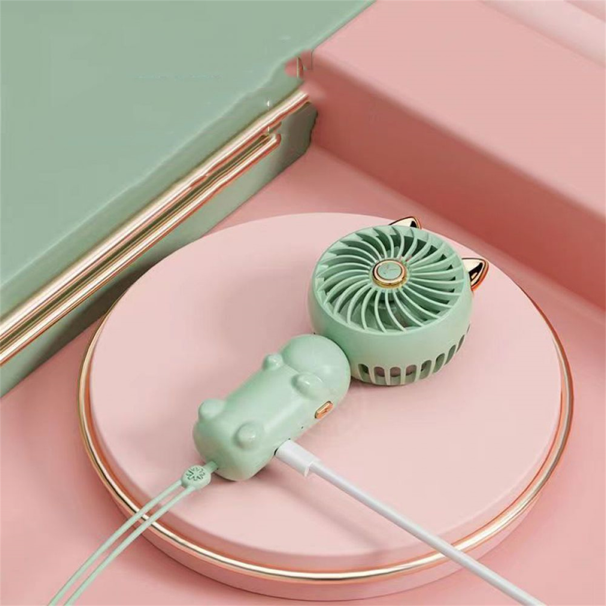 Zwei katzenförmige Ventilatoren auf rosa Oberfläche. Einer separat, einer mit Ladekabel verbunden.