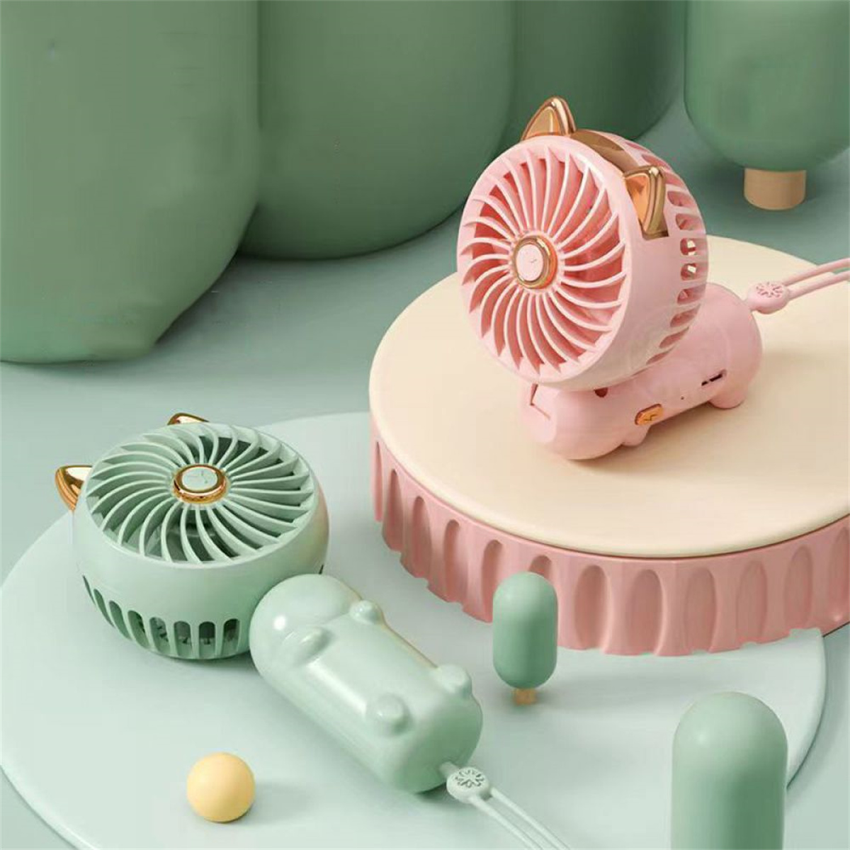 Rosa katzenförmiger Ventilator mit Ohren und zwei grüne Ventilatoren. Die Ventilatoren sind auf hellem Untergrund.