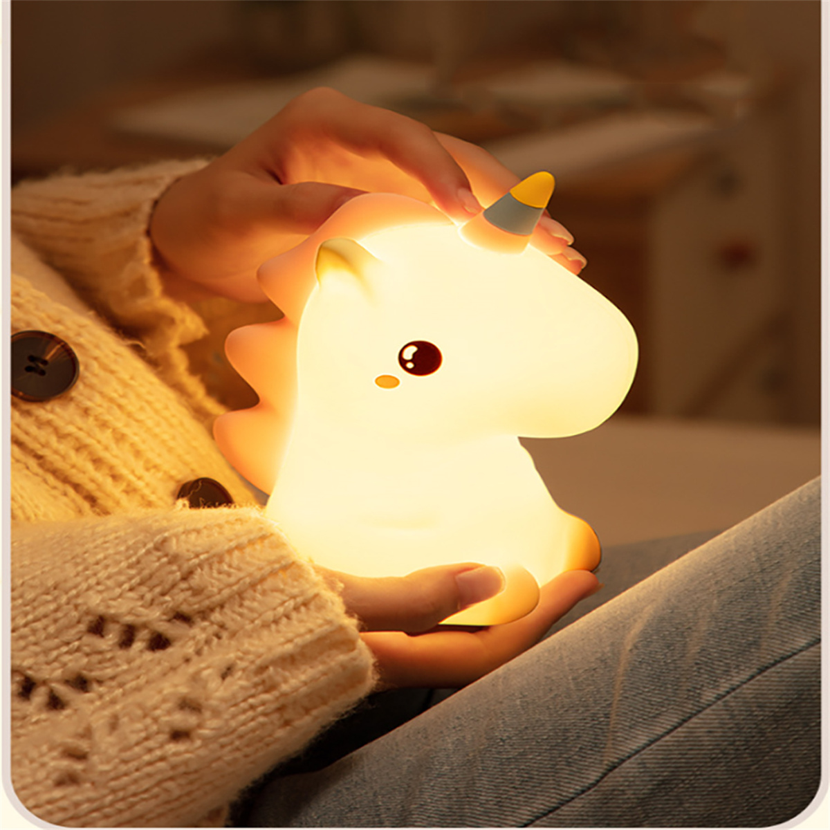 Ein beleuchtetes Einhorn-Nachtlicht wird von einer Person gehalten. Die Person trägt einen Pullover.