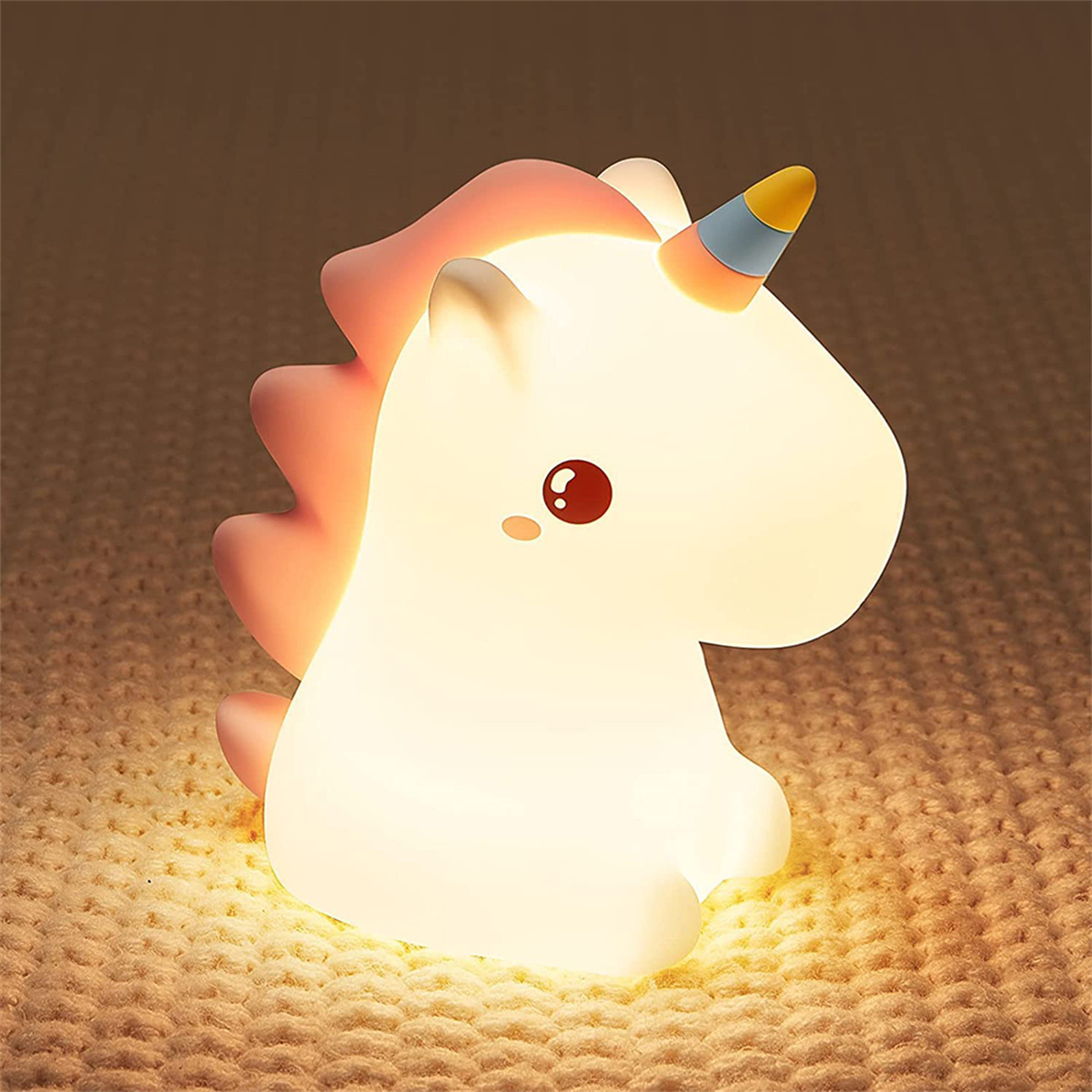 Ein Einhorn-Nachtlicht. Es leuchtet und hat rosa, weiße und gelbe Farben. Es befindet sich auf einer gestrickten Oberfläche.