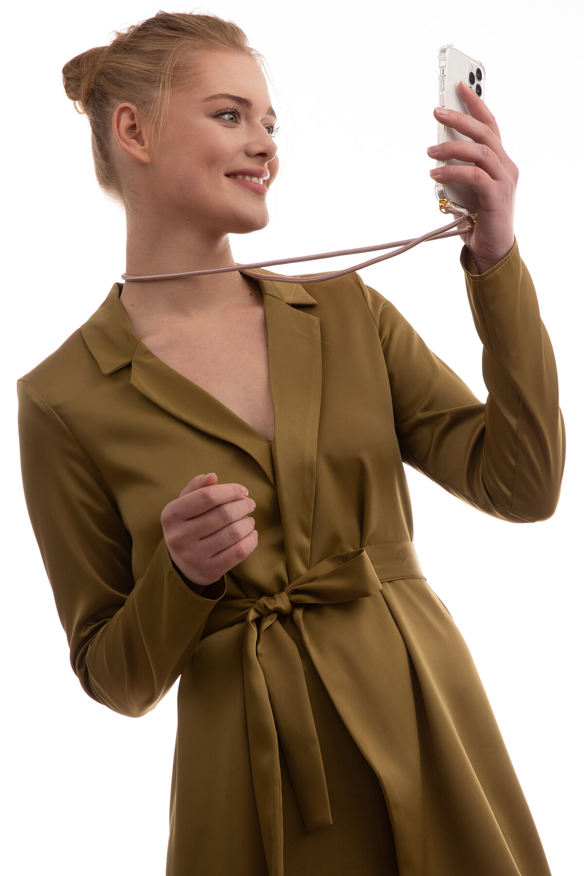 Lächelnde Frau, die ein Handy mit Umhängeband hochhält. Sie trägt ein grünes Kleid.