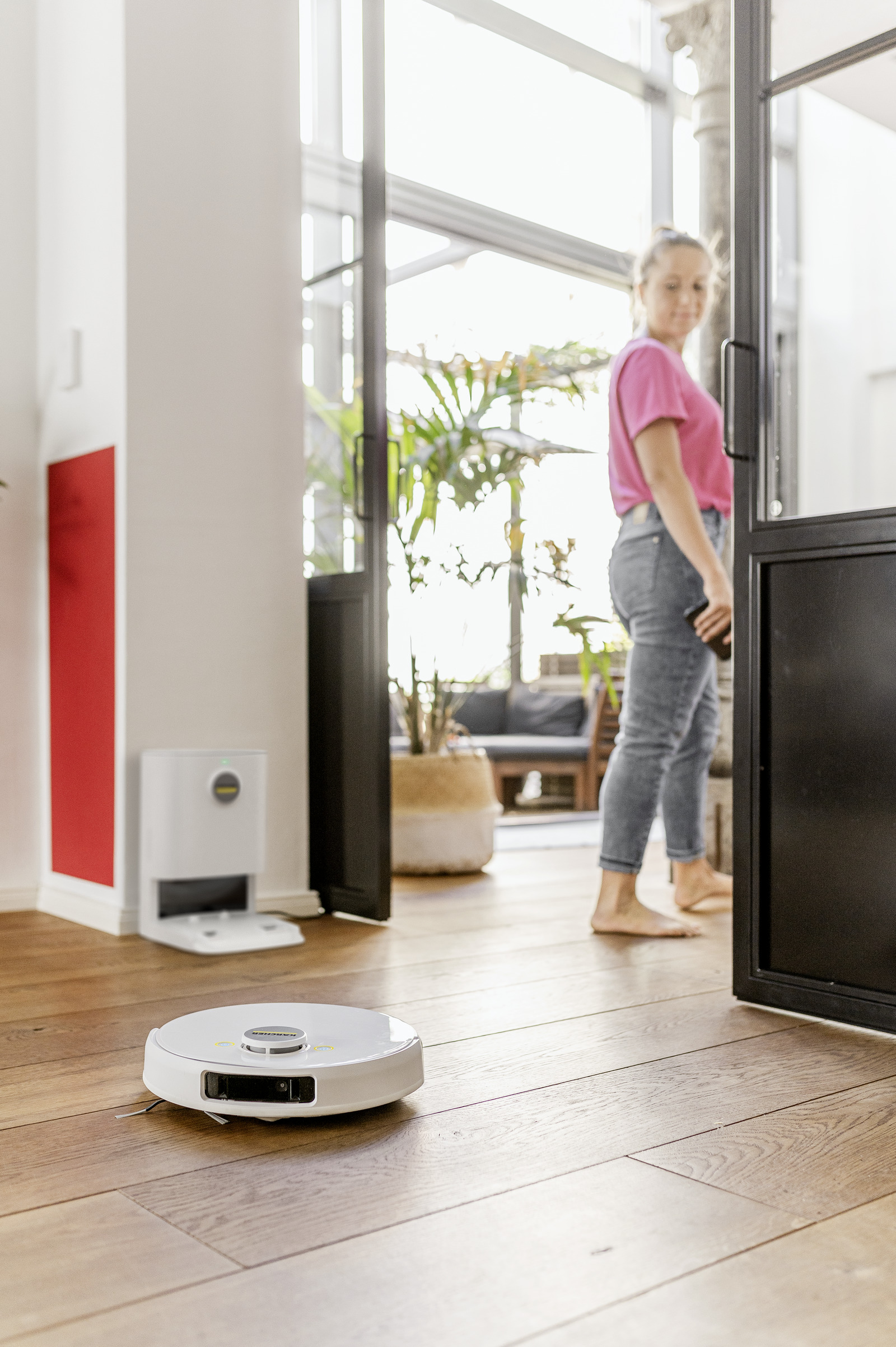 Aspirapolvere robot che pulisce un pavimento in legno. Una donna è in piedi vicino.