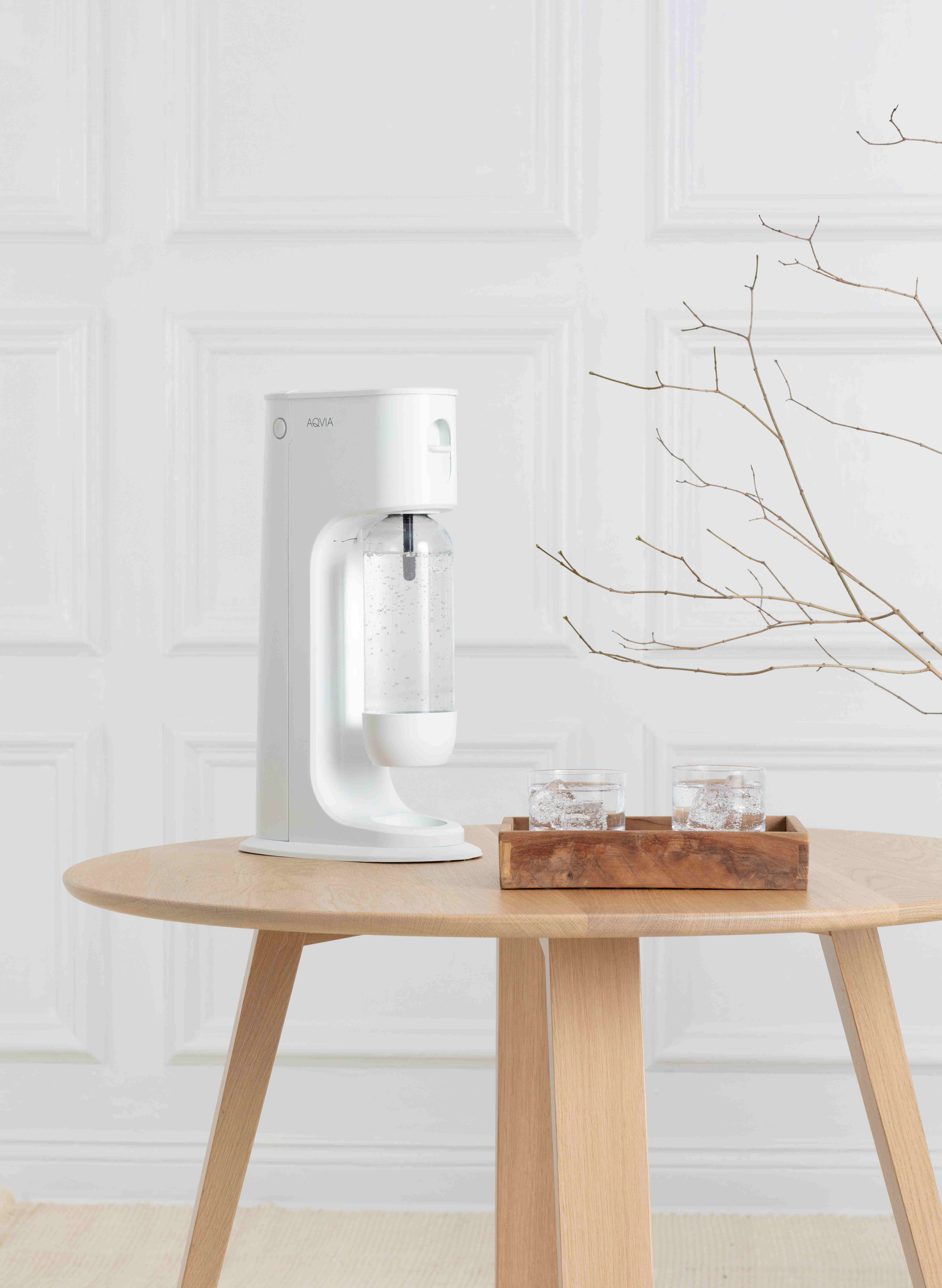 Weißes Wasserfiltergerät auf einem Holztisch mit zwei Gläsern Wasser und einem Astdekor.