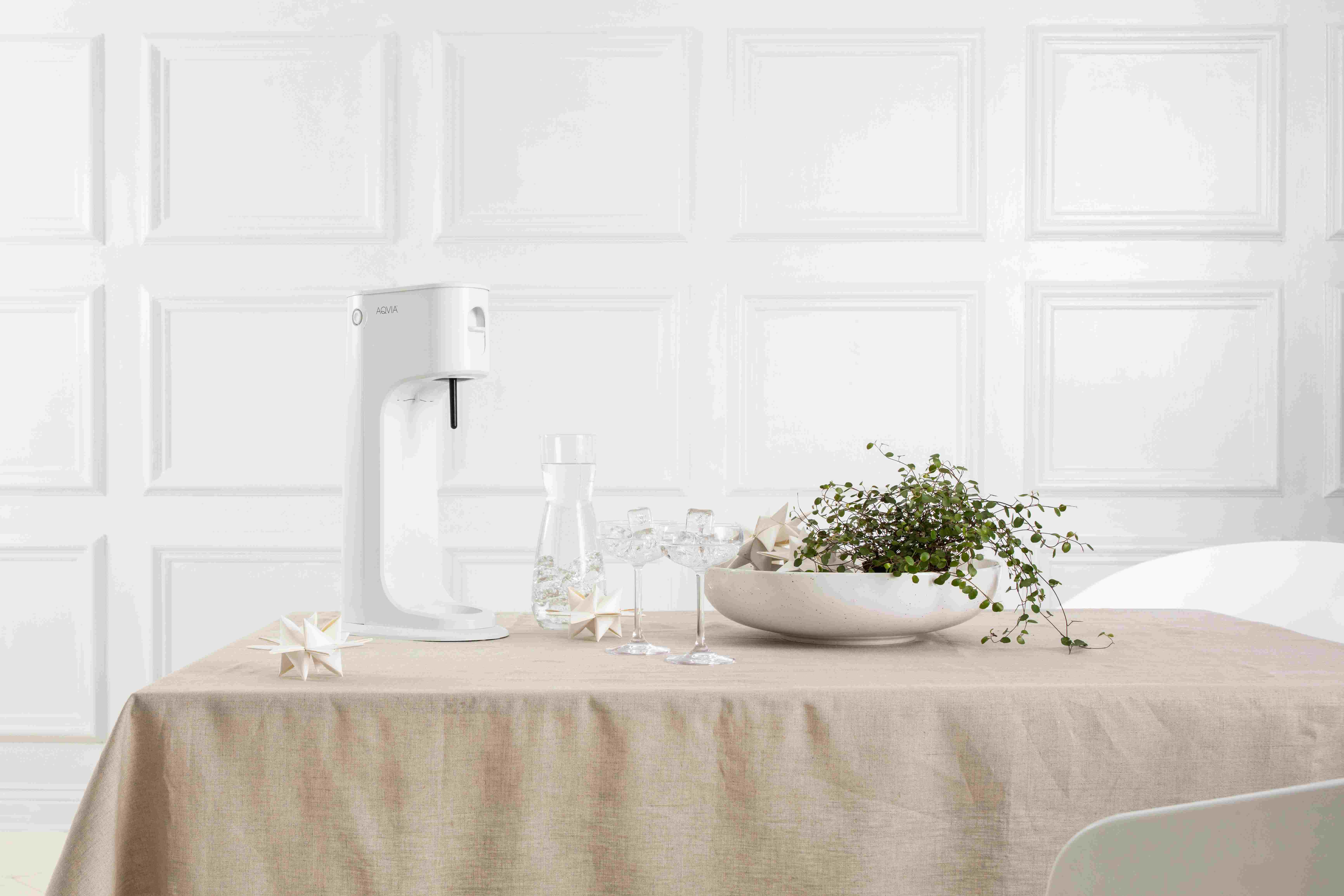 Ein weißer Wasserspender und Tischdecke mit Pflanze im Vordergrund.