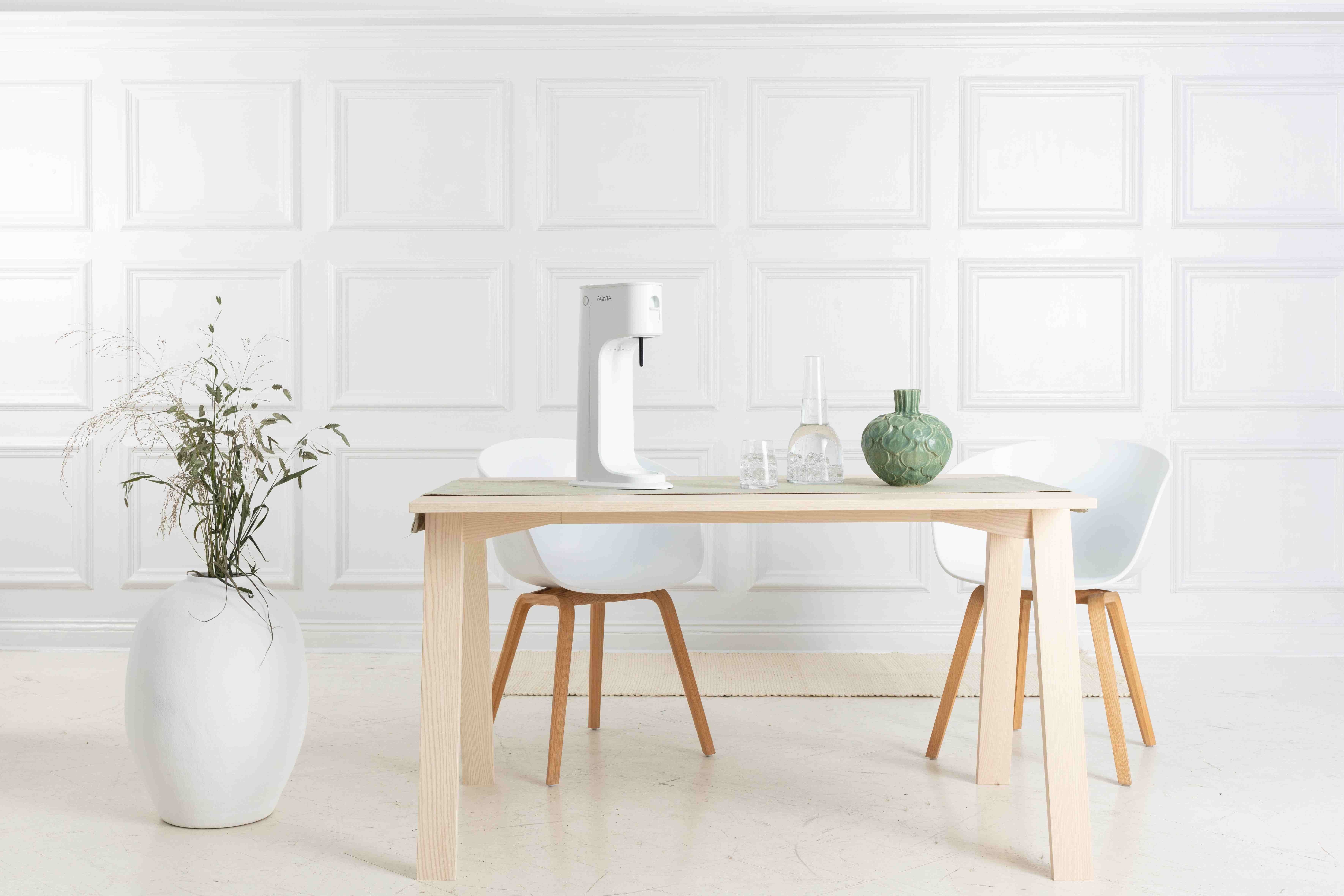 Ein modernes, minimalistisches Esszimmer mit weißem Tisch, Stühlen und einem Spender vor einer weißen Wand.