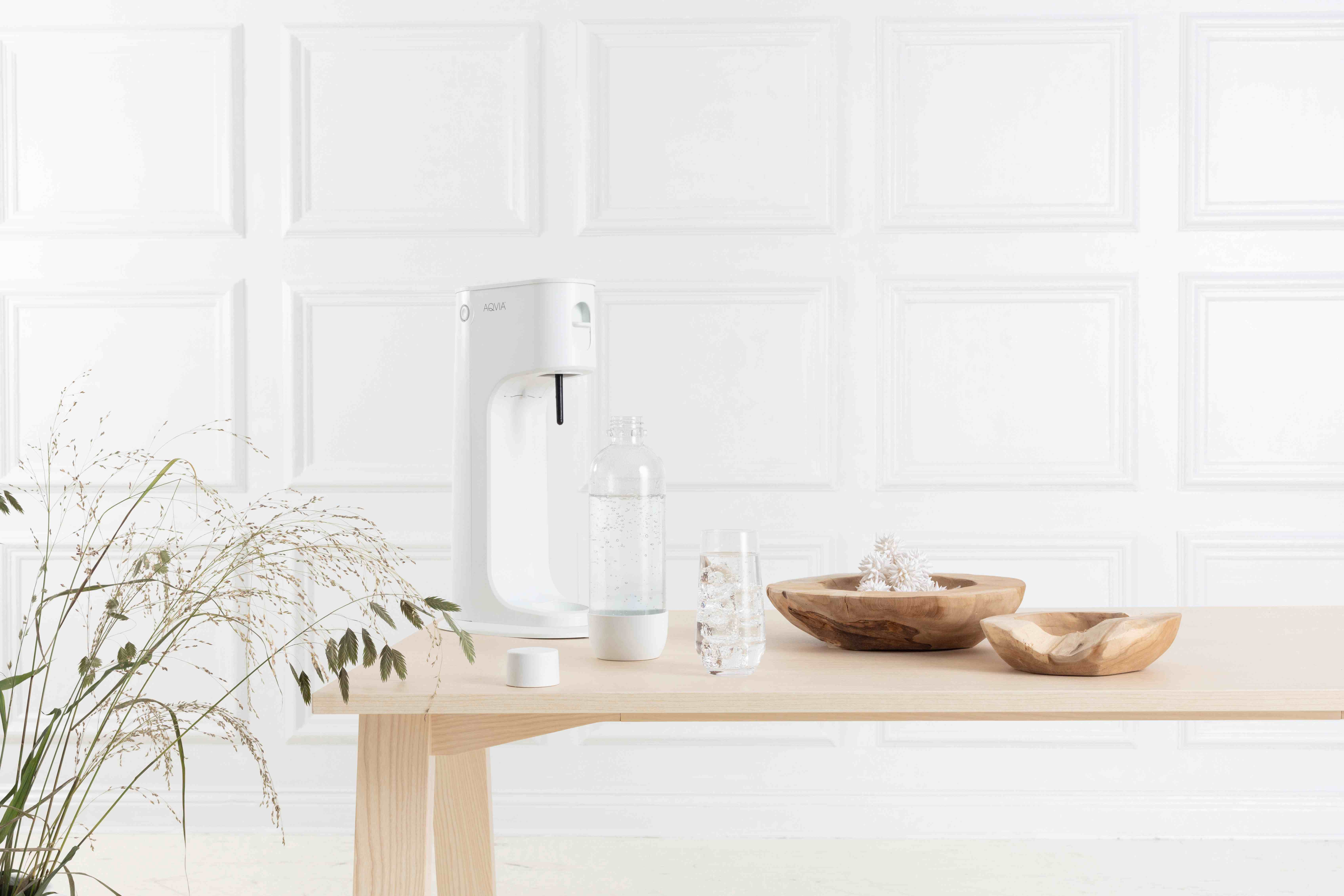 Weißer Wasserfilter mit einem Glas, einer Flasche und Holzschalen auf einem Holztisch.