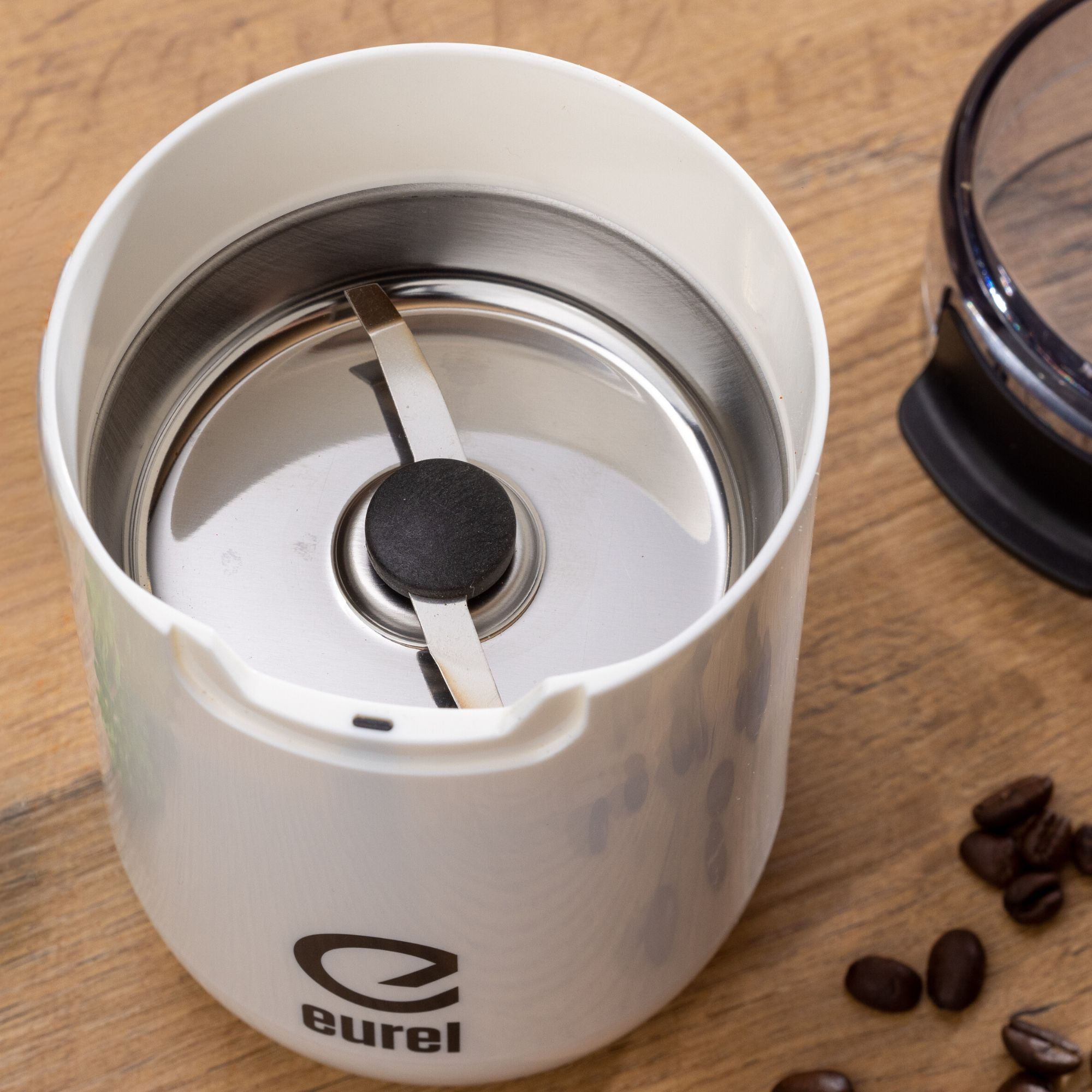 Weiße Kaffeemühle mit einer Edelstahlklinge im Inneren. Kaffeebohnen drumherum.