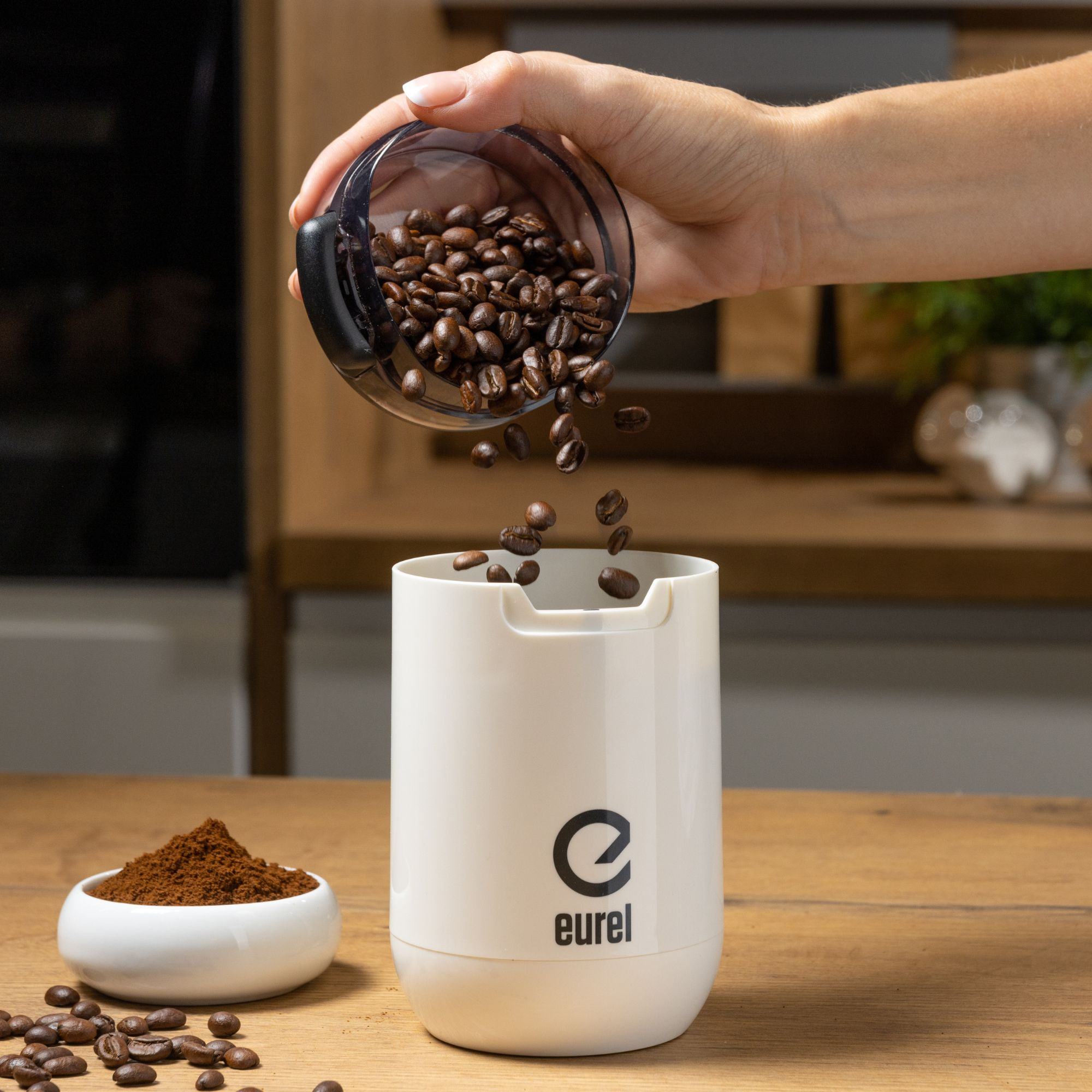 Eine Person gießt Kaffeebohnen in eine Mühle. Eine Schüssel mit Kaffeesatz daneben.
