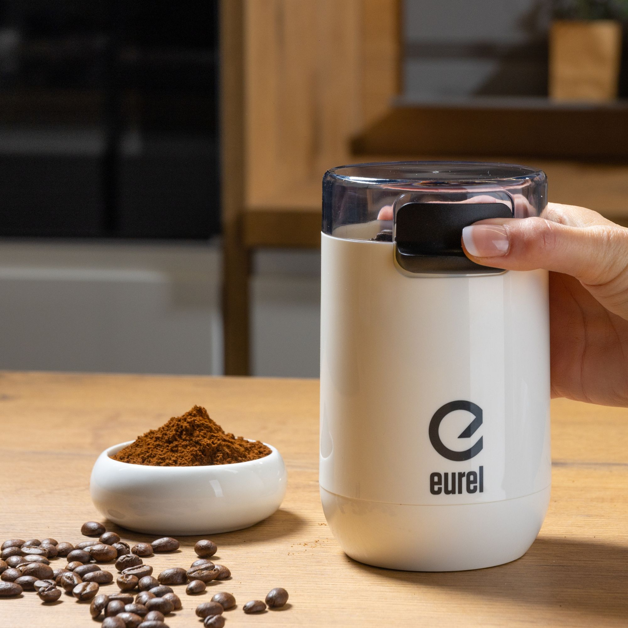 Weißer Kaffeemühle mit schwarzem Deckel. Einige Kaffeebohnen und gemahlener Kaffee sind sichtbar.