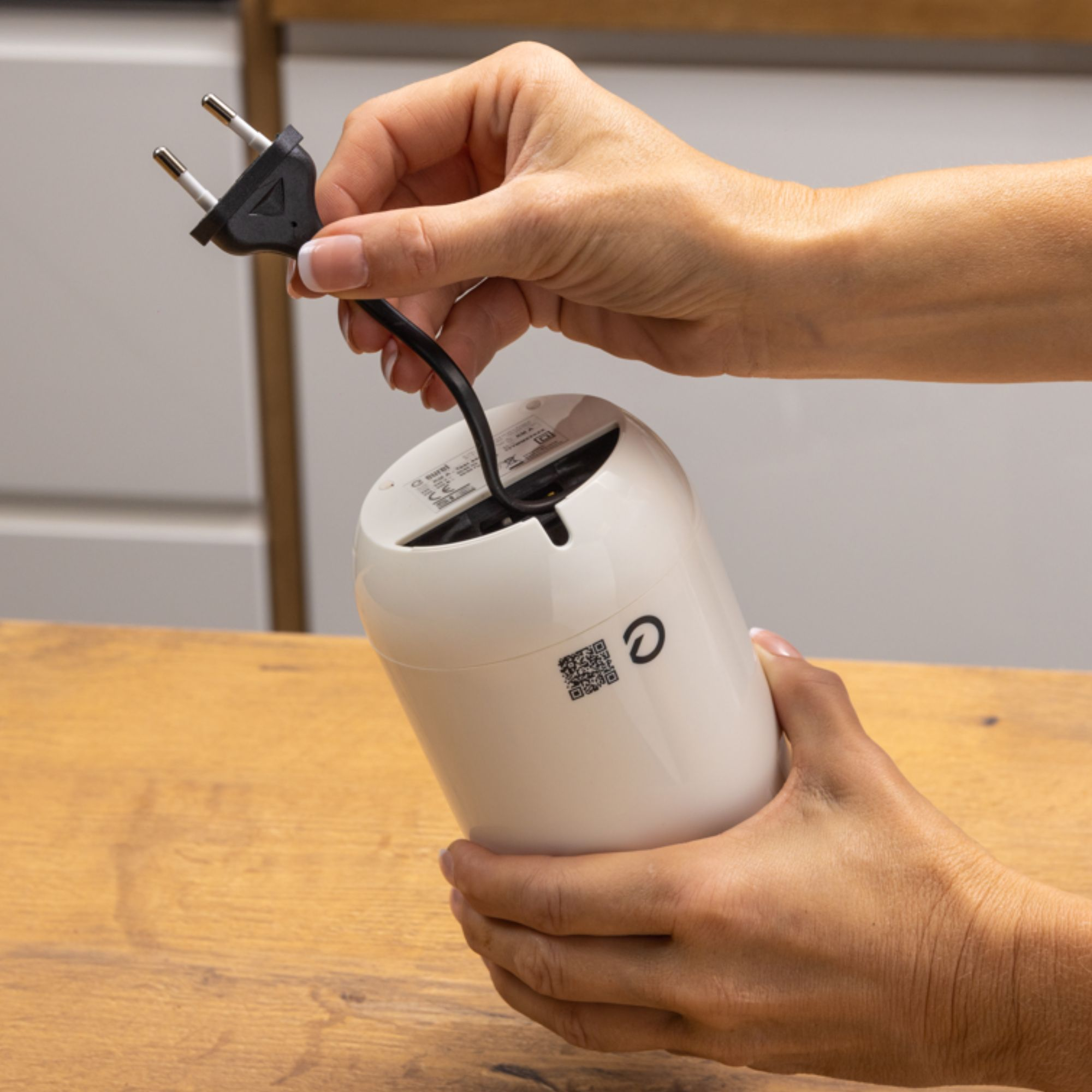 Hände einer Person, die einen weißen Zylinder halten. Ein Stecker wird hineingesteckt.