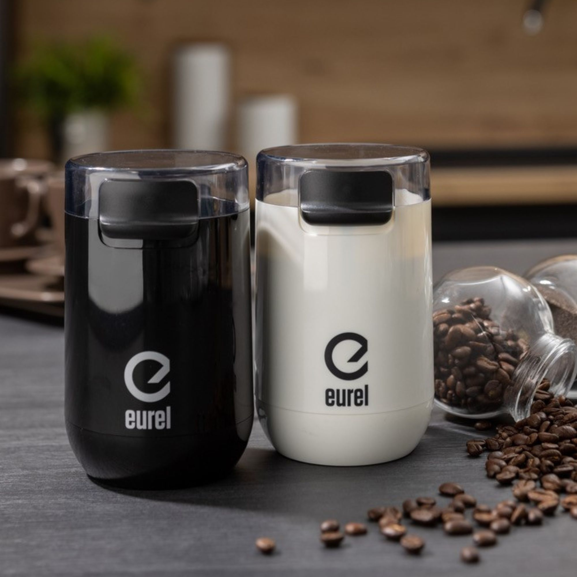 Zwei elektrische Kaffeemühlen, schwarz und weiß, mit der Marke 'eurel'. Kaffeebohnen sind verstreut.
