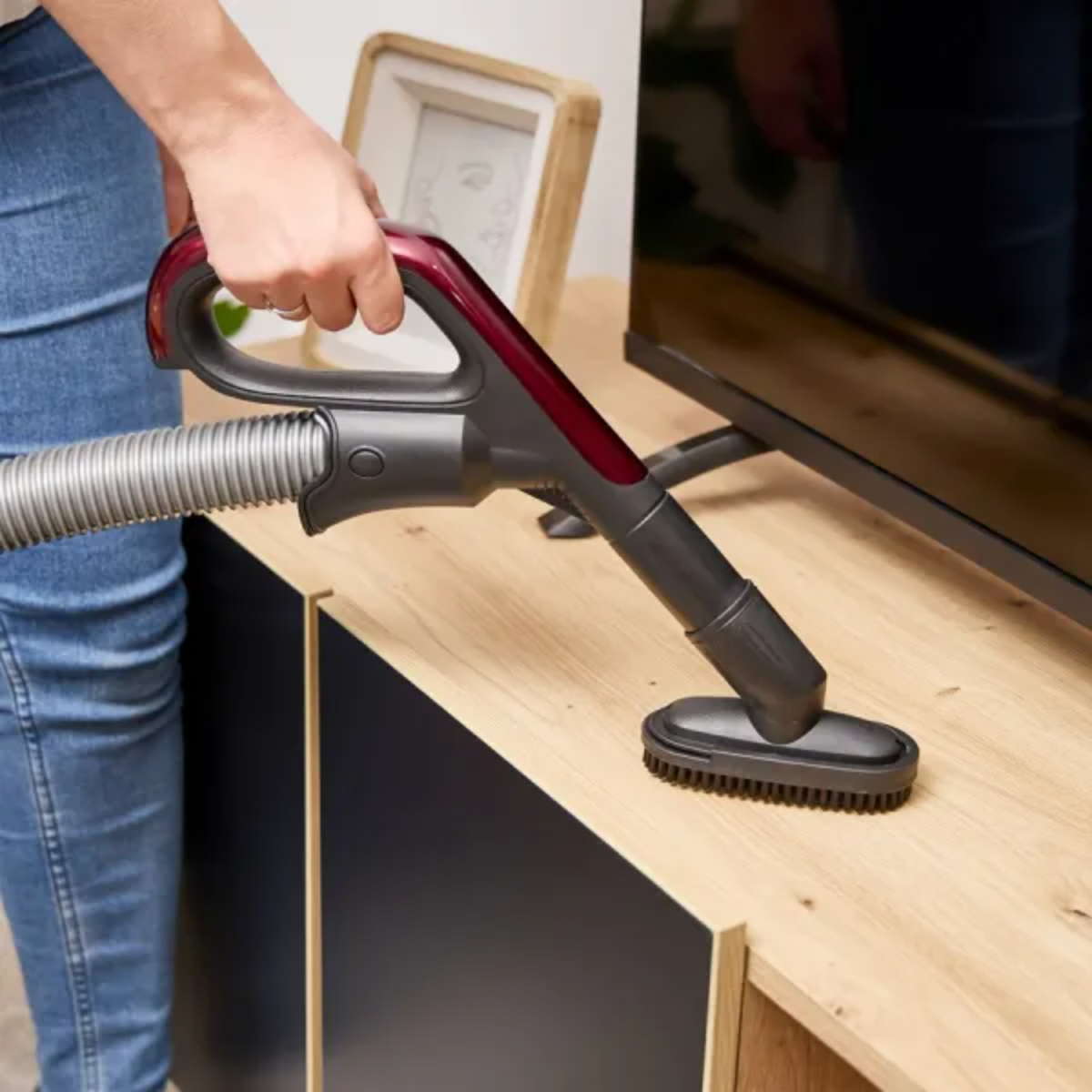 Person reinigt Holzschrank mit Staubsaugeraufsatz.