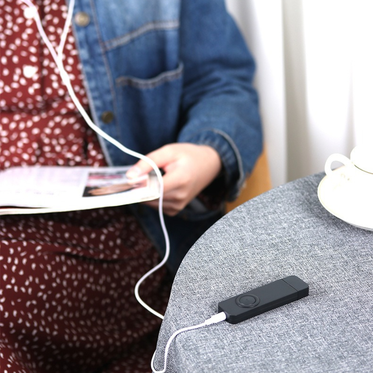 Eine Frau mit Jeansjacke hört Musik über ein kleines schwarzes Gerät mit Kopfhörern.