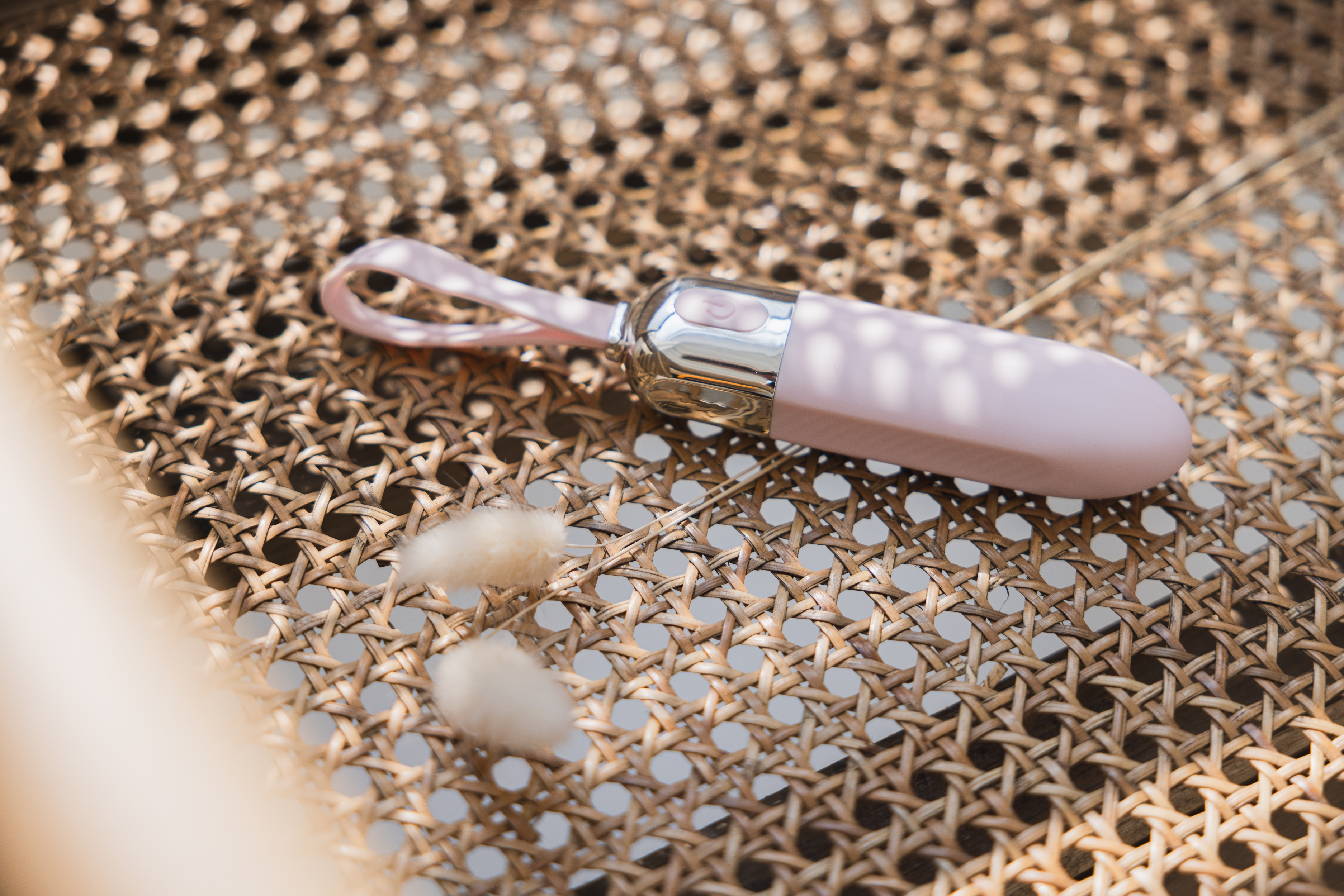 Ein pinkfarbener und silberner Vibrator auf gewebter Oberfläche, mit Blumen.