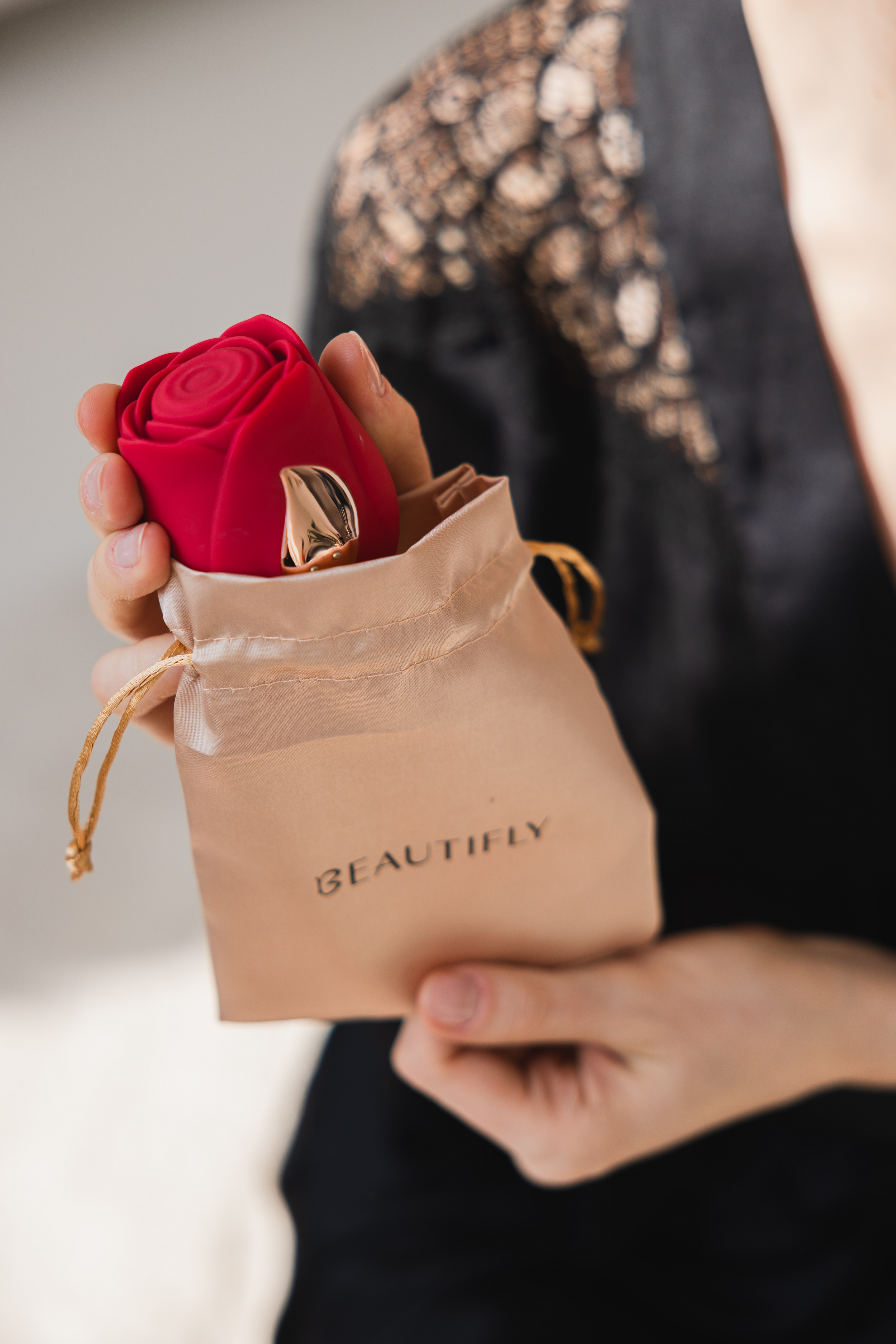 Osoba trzymająca urządzenie w kształcie róży w beżowej torbie. Urządzenie ma złote akcenty.